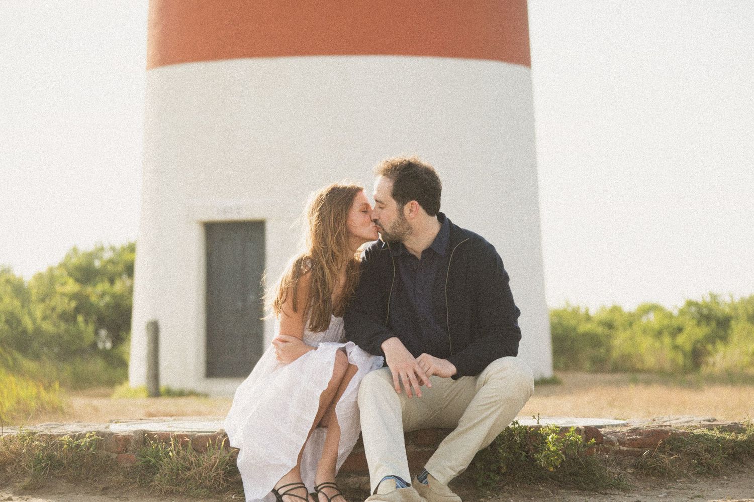 Intimate moment shared between couple at lighthouse during golden hour.
