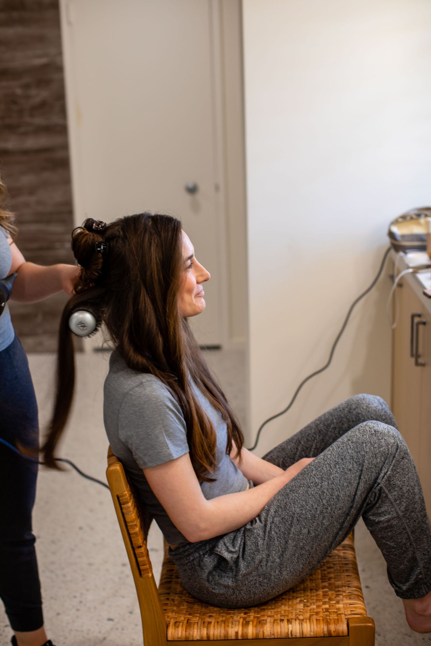 Person getting their hair styled while sitting in a wooden chair.