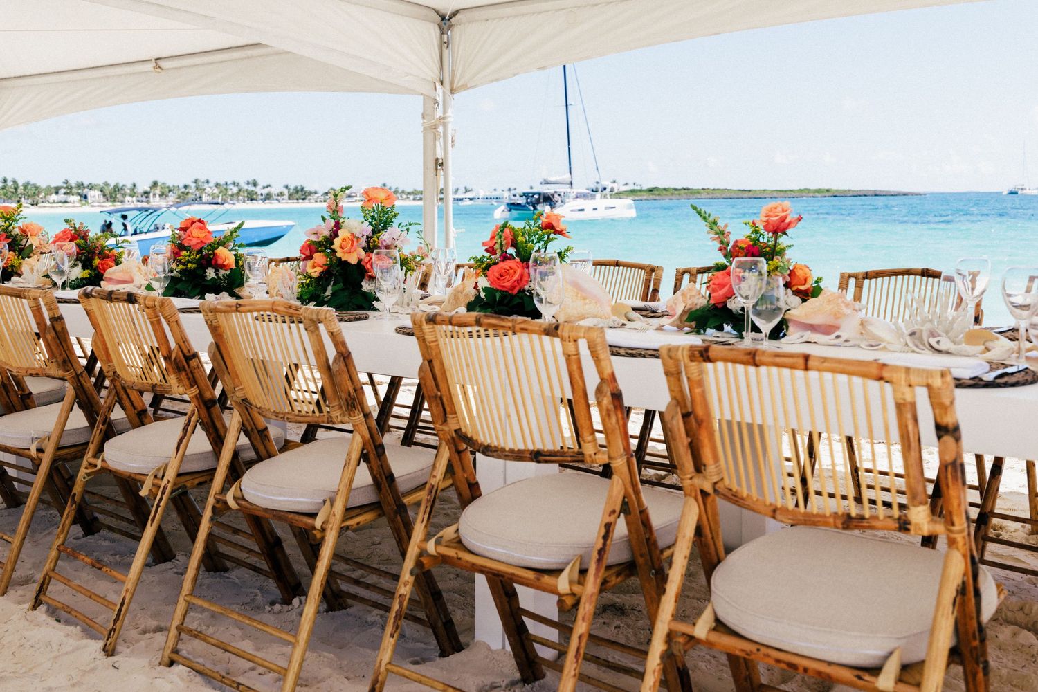 Outdoor beach wedding reception setup with wooden chairs and ocean views.