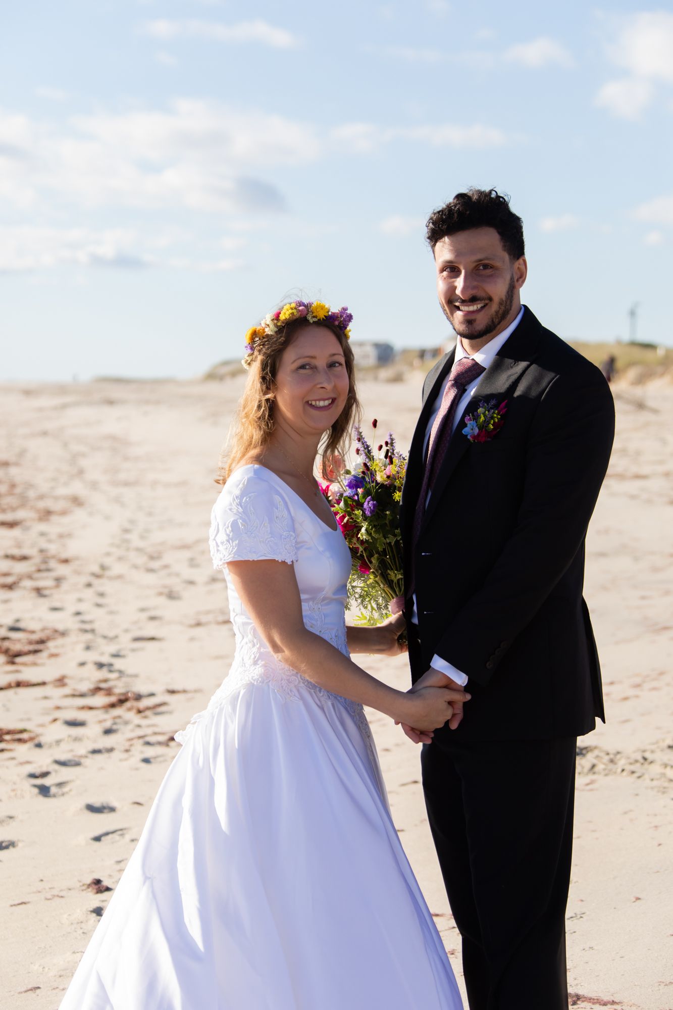 Newlyweds sharing a romantic moment on the beach with colorful wildflower bouquet.