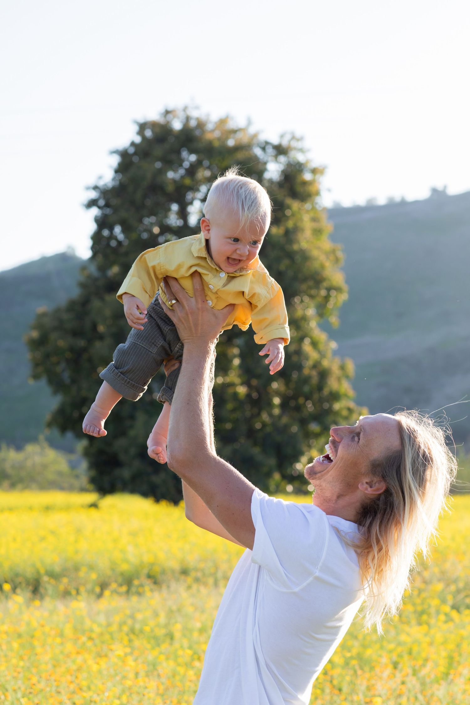 Playful moment of lifting and spinning in a sunlit meadow of yellow flowers.