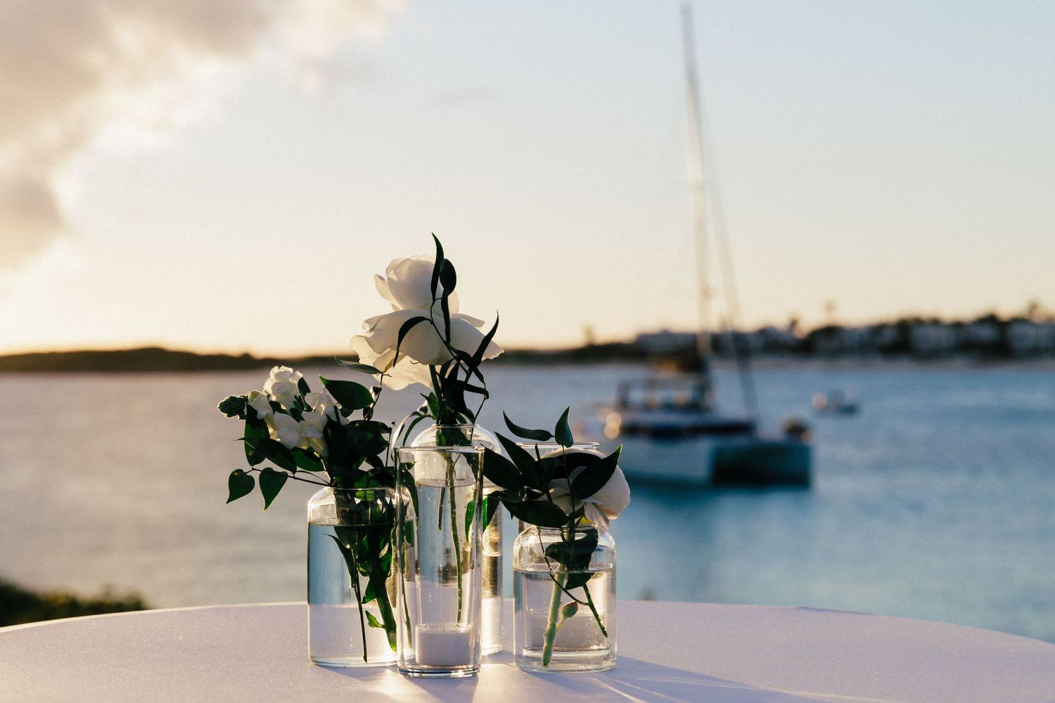 Elegant floral centerpiece in glass vases with sailboats in background at waterfront venue.