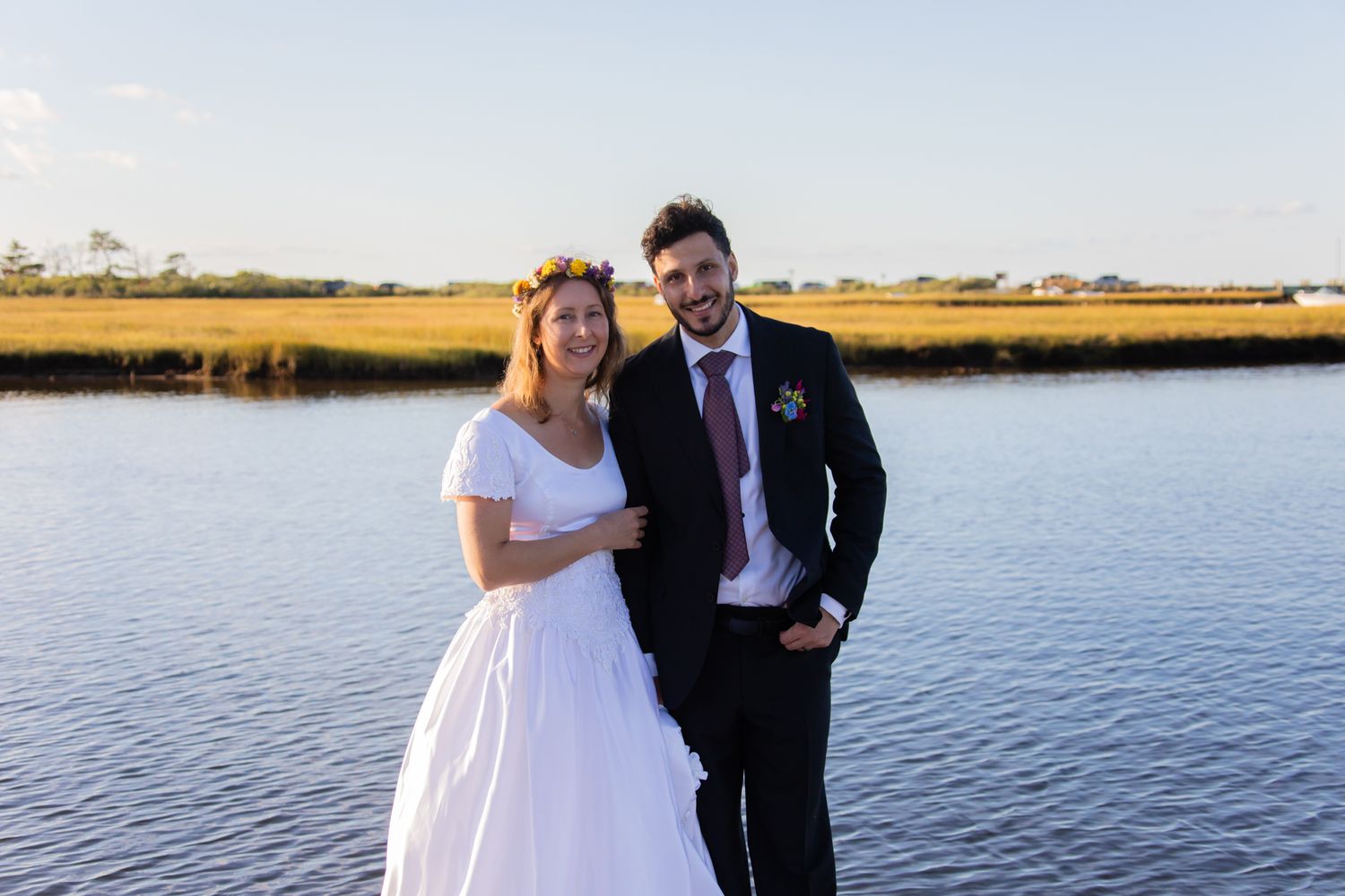 A wedding couple poses together against a serene waterfront backdrop.