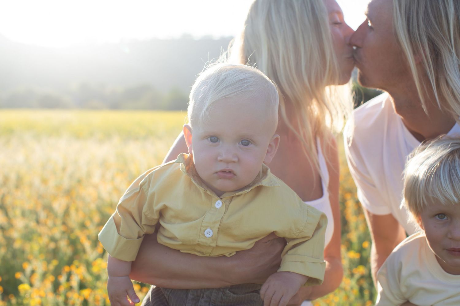A tender family moment captured in a sunlit meadow of yellow flowers.
