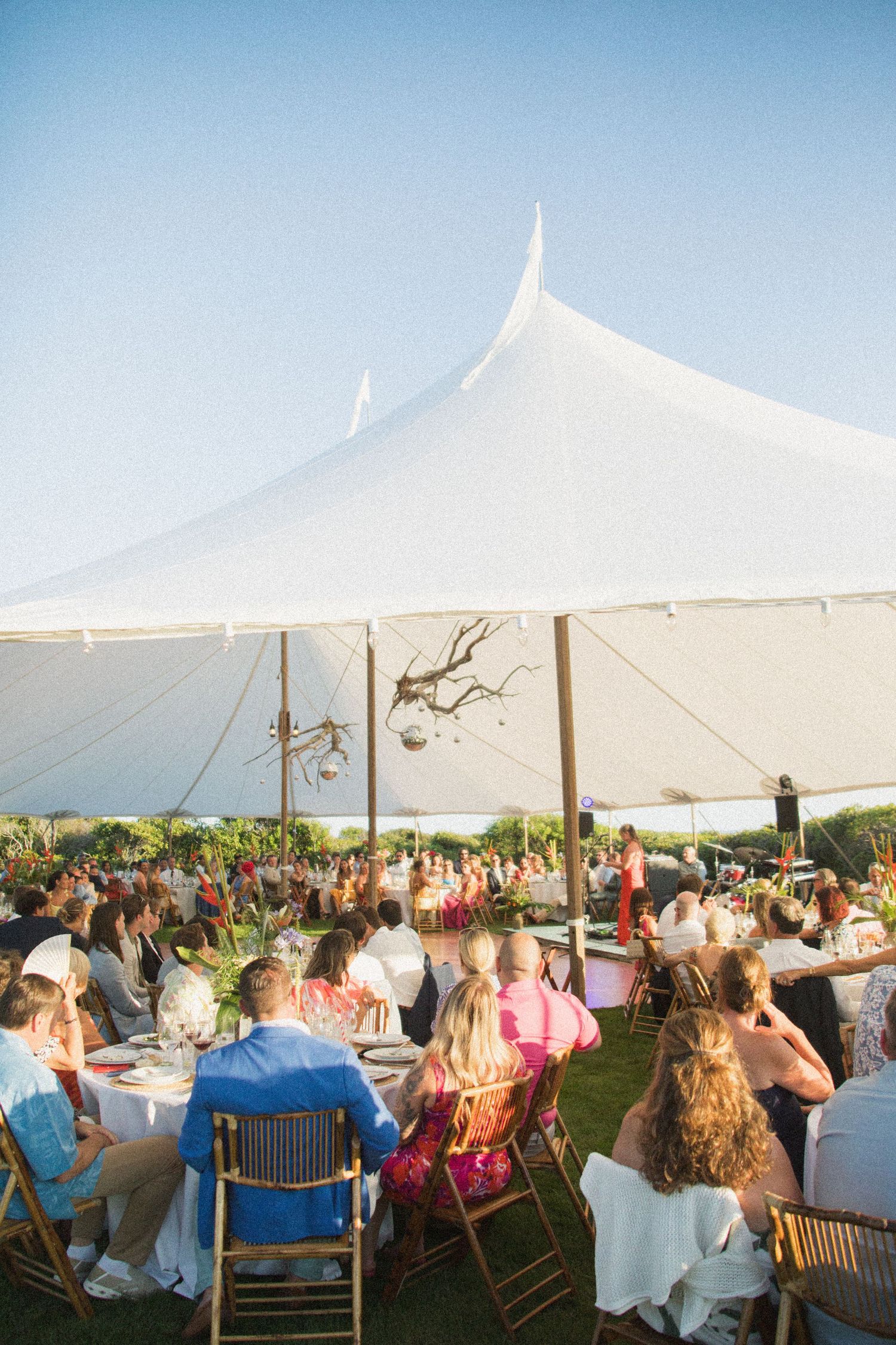 Guests seated under a white tent canopy at a seaside wedding reception.