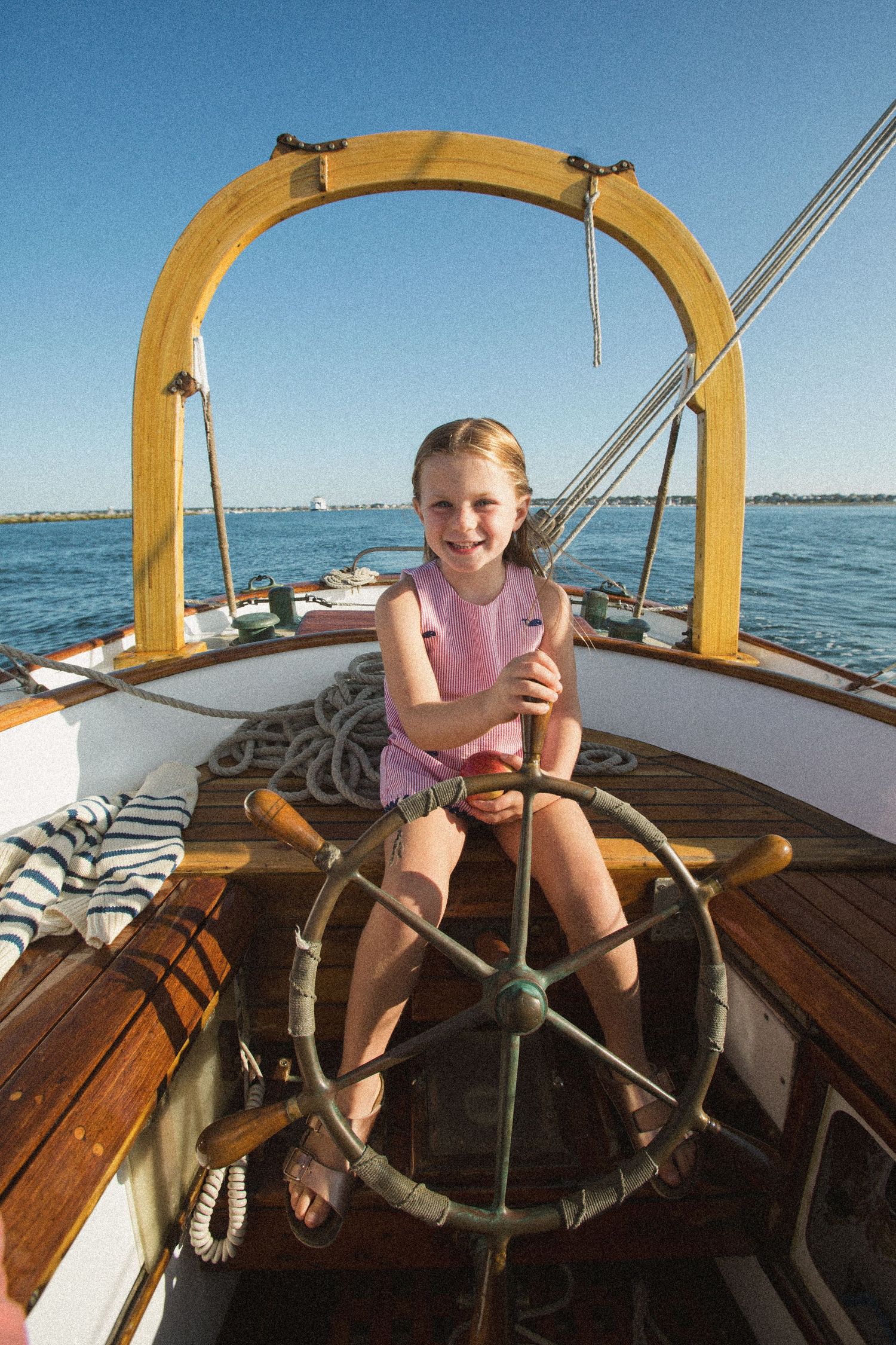 Young sailor at the wooden helm of a classic boat with yellow arch frame.