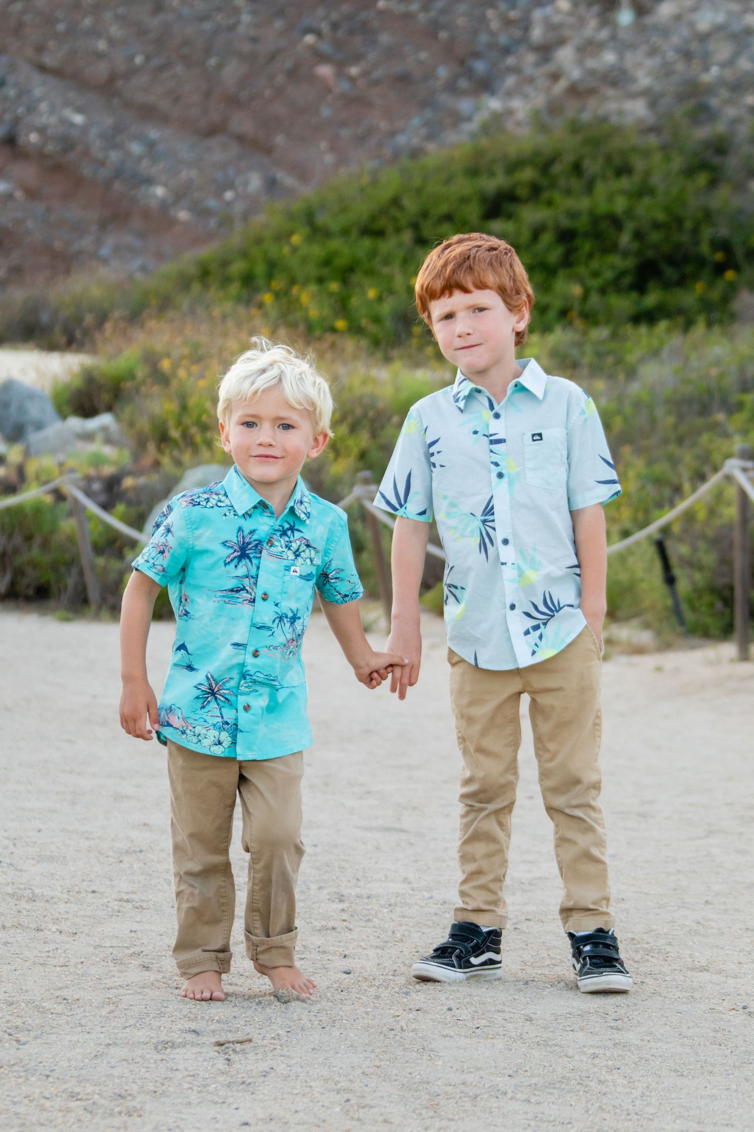 Children in matching outfits walking on sandy beach near cliffs.