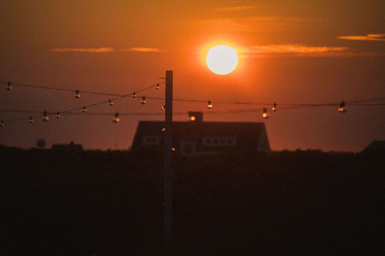 Vibrant orange sunset over a horizon with string lights silhouetted against the darkening sky.