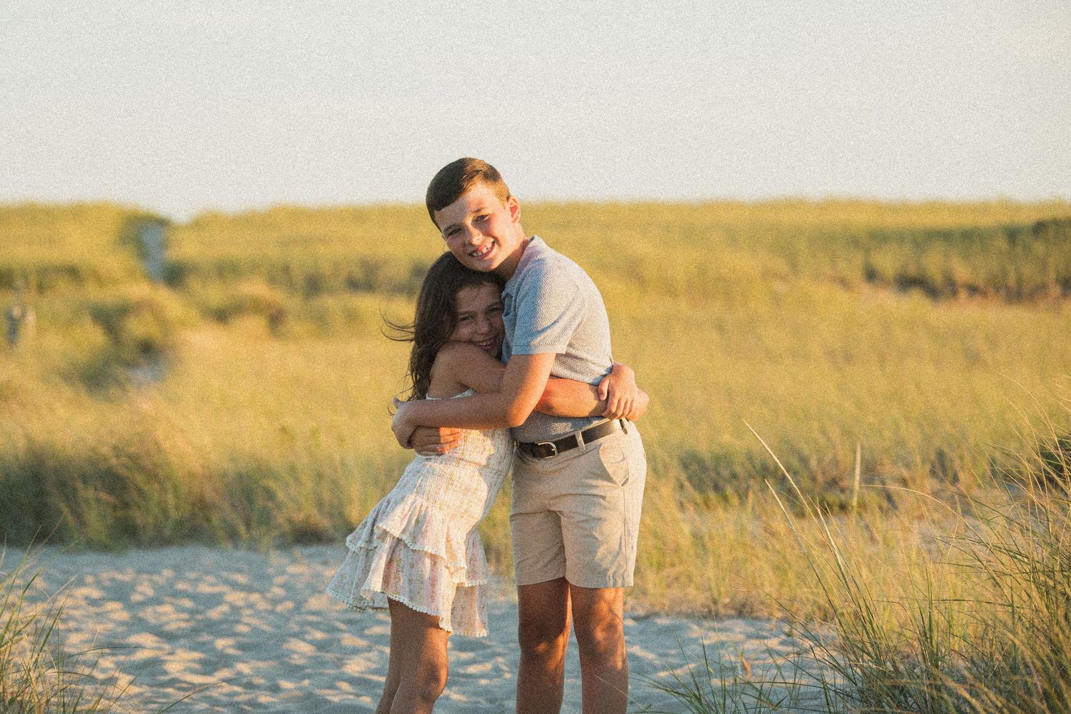 A tender embrace captured in warm lighting among coastal dunes.