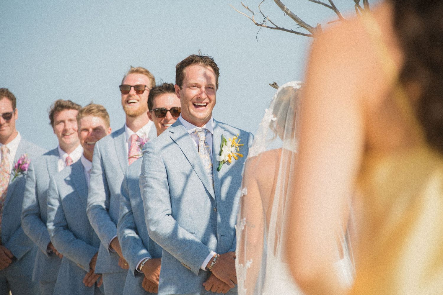 Wedding party in light blue suits gathered on the beach.
