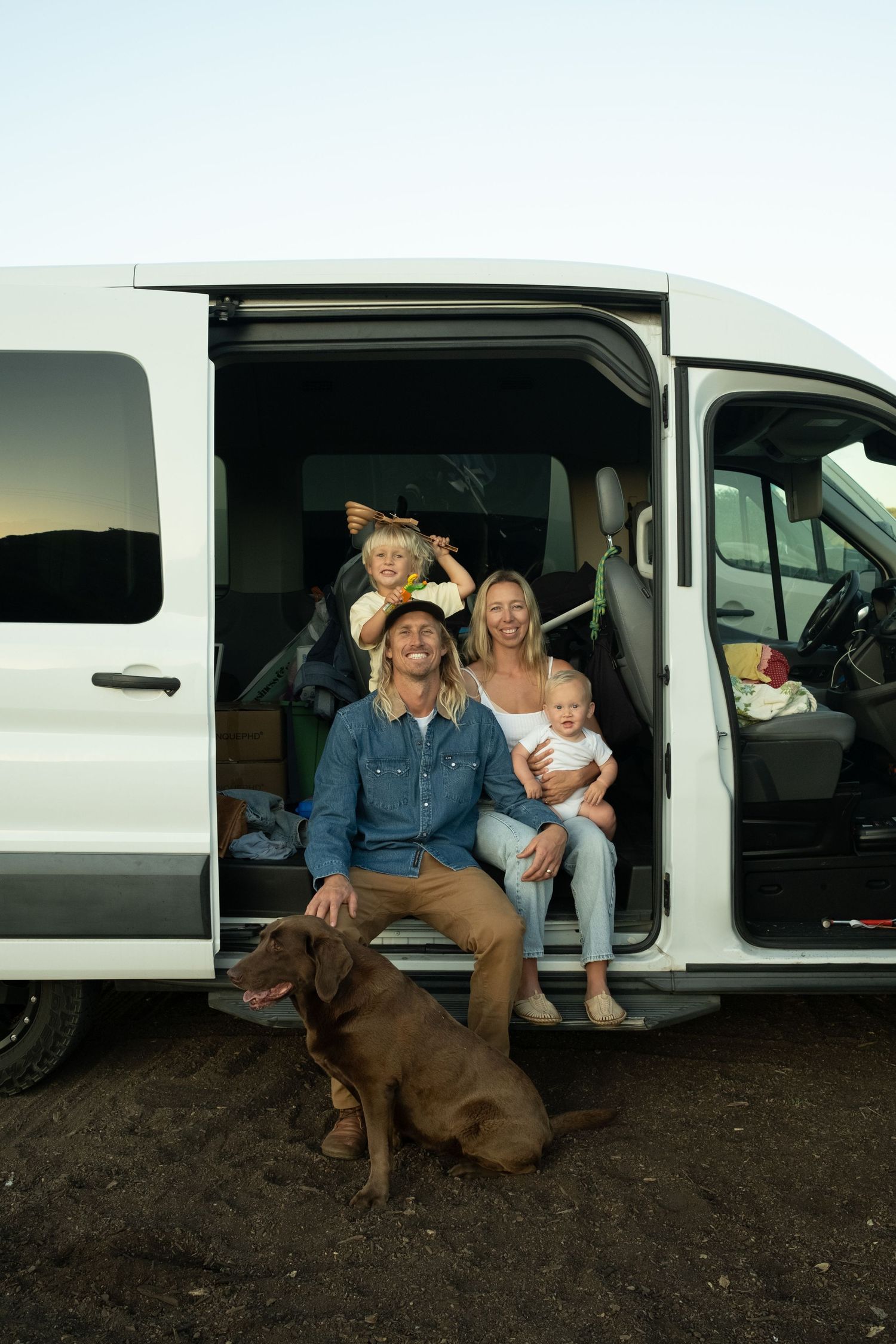 Family sitting in white van with their dog, casual outdoor lifestyle photo.