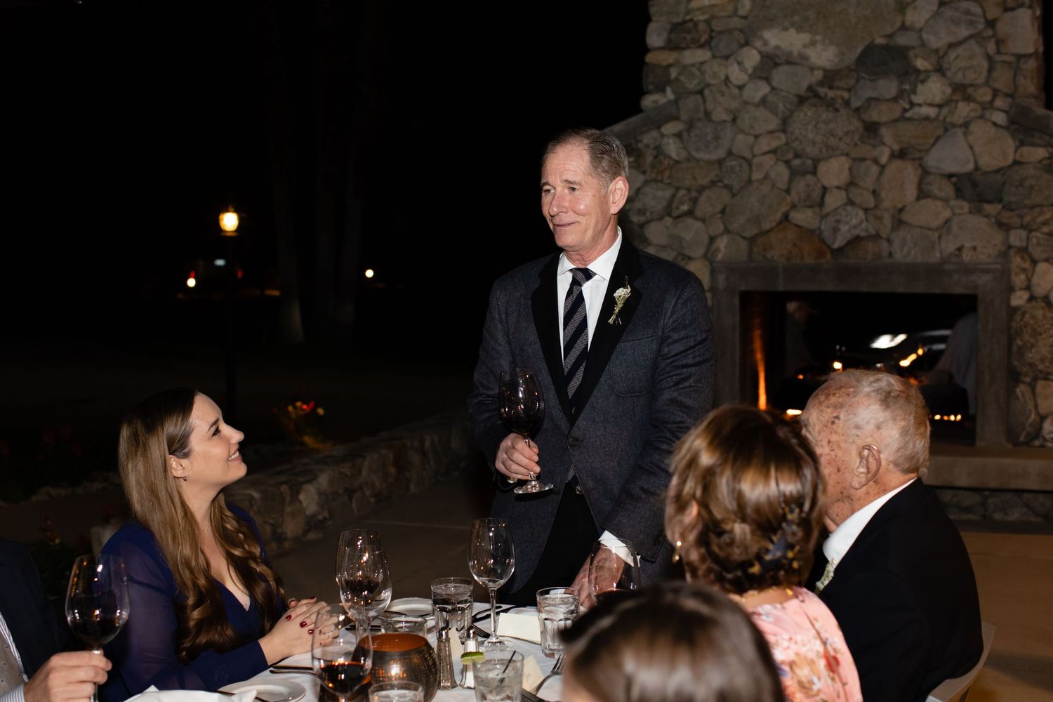 Guests seated at an elegant dinner party with stone walls and ambient lighting.