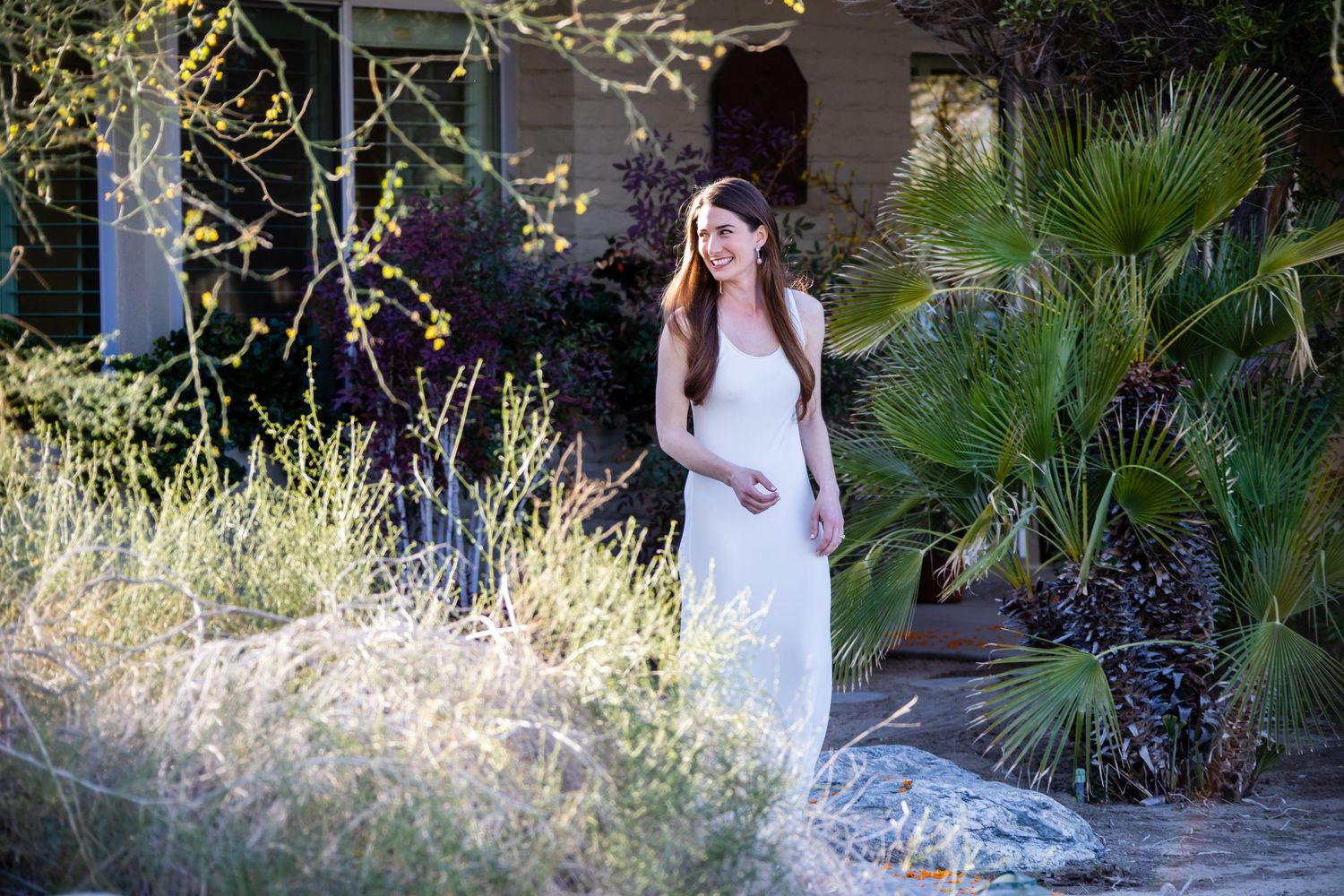 Figure in white dress standing among desert plants at sunset.