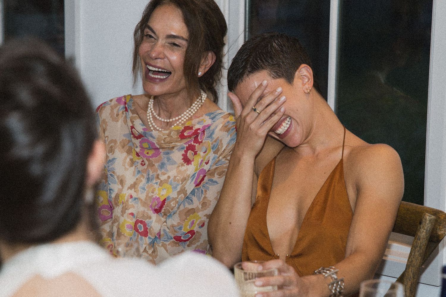Two women laughing joyfully at a social gathering, one covering her face with her hand in amusement.