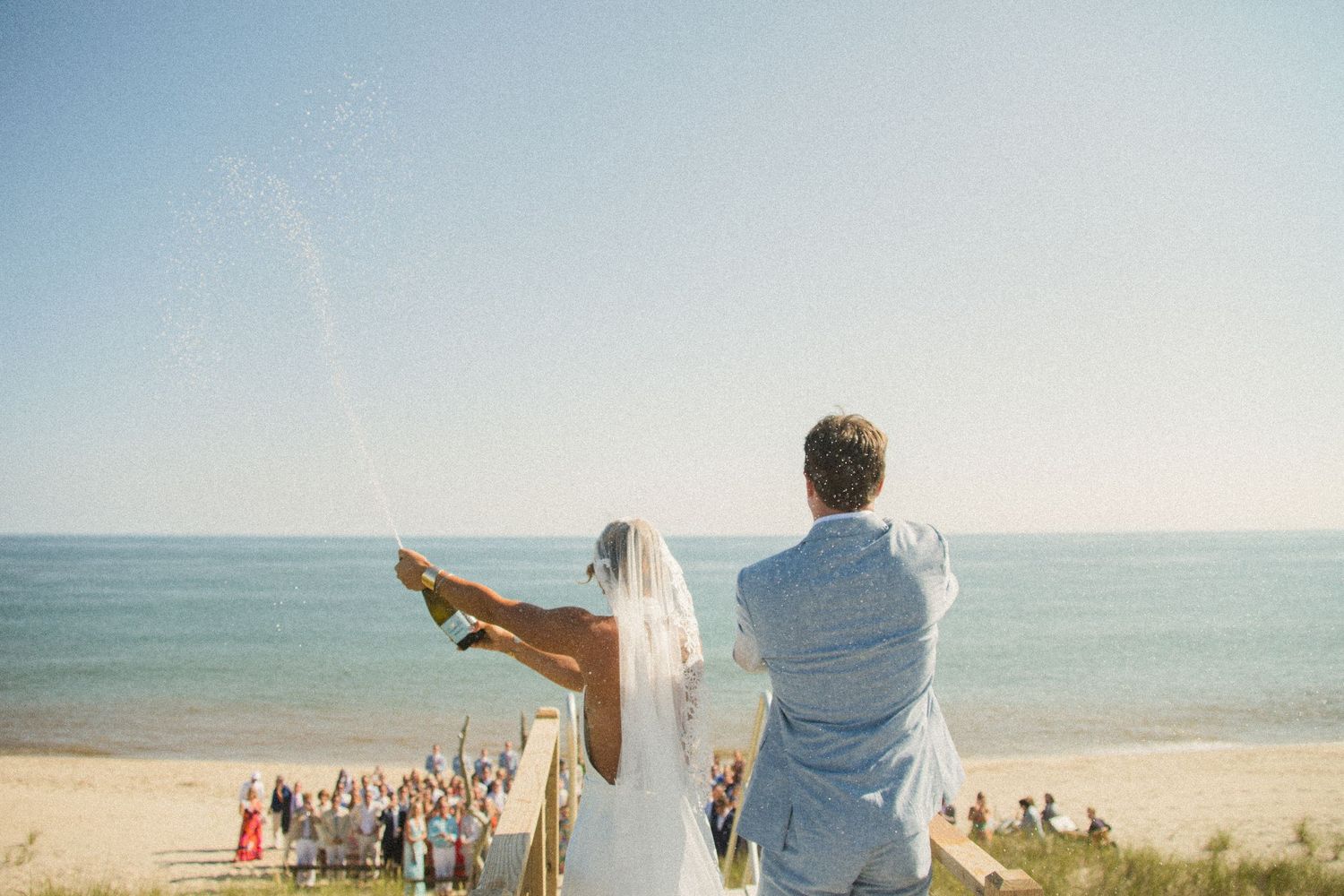 A couple in wedding attire stands on a beach overlooking the ocean during their destination ceremony.