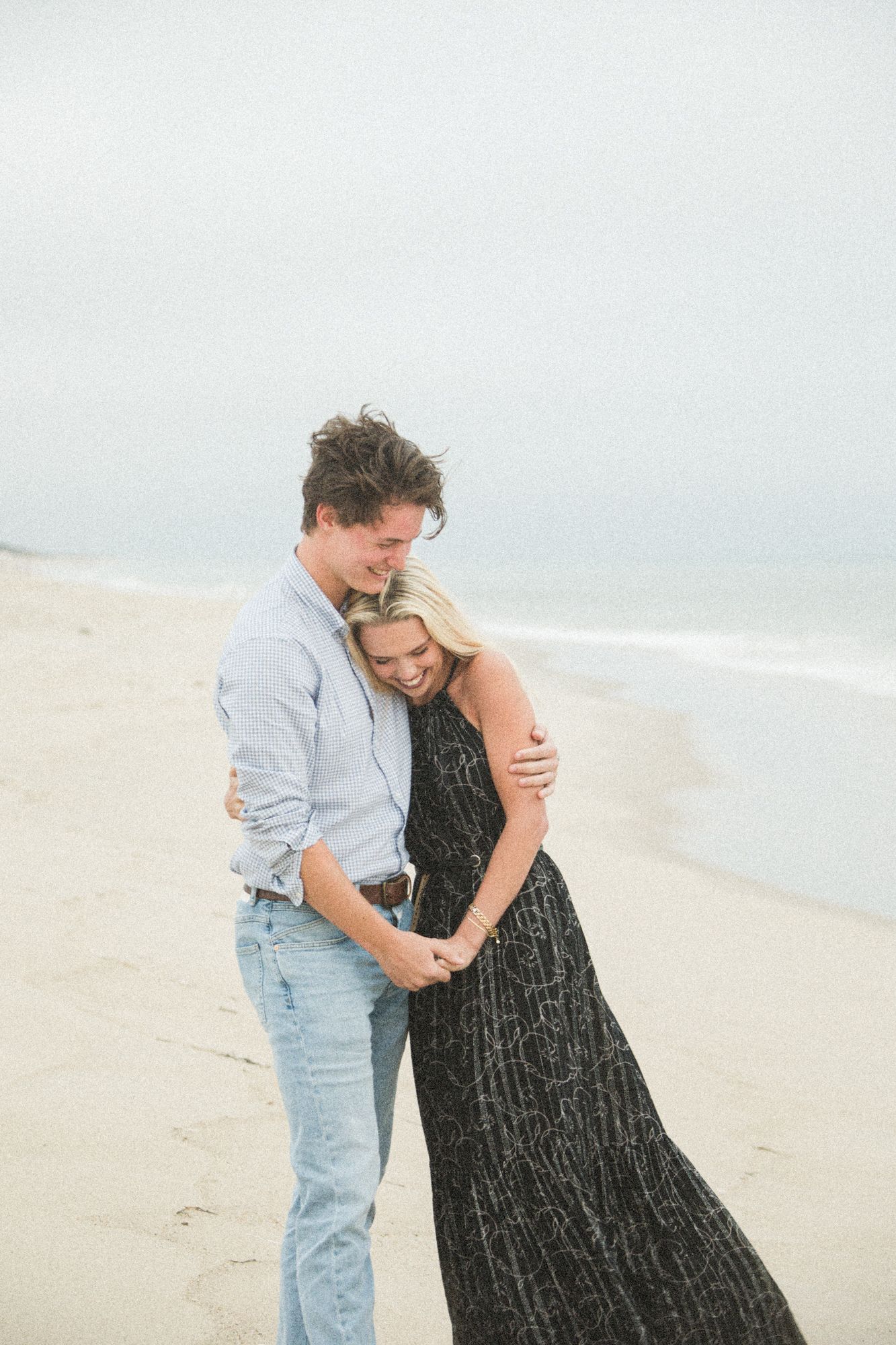 A couple embraces on a misty beach, with the woman wearing a black dress.