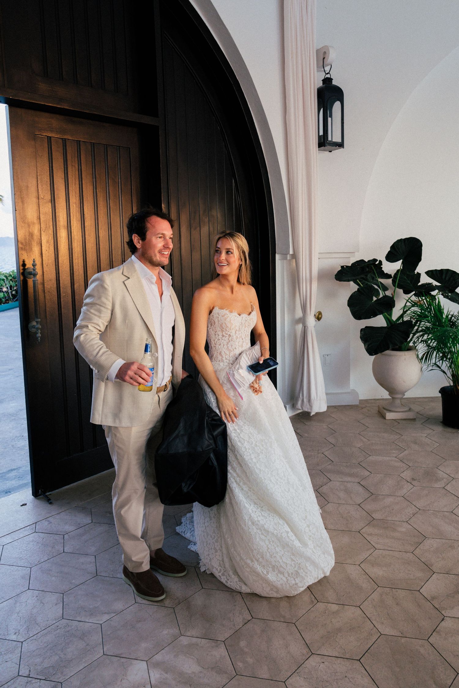 Newlyweds share a playful moment under an arched walkway with stone flooring at a tropical venue.