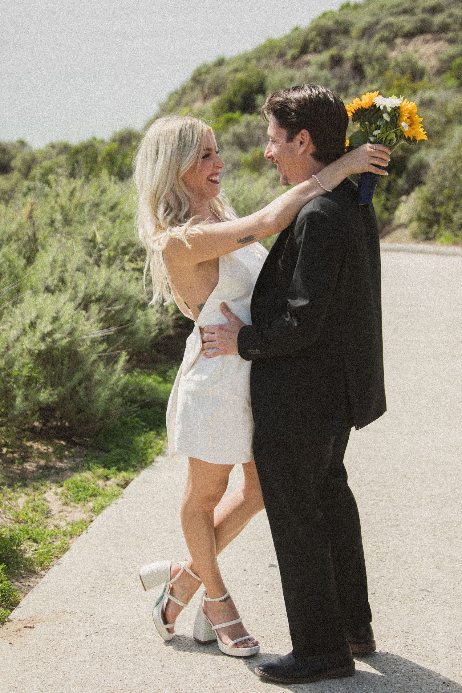 Joyful wedding couple shares a fun dance moment on a scenic coastal trail.