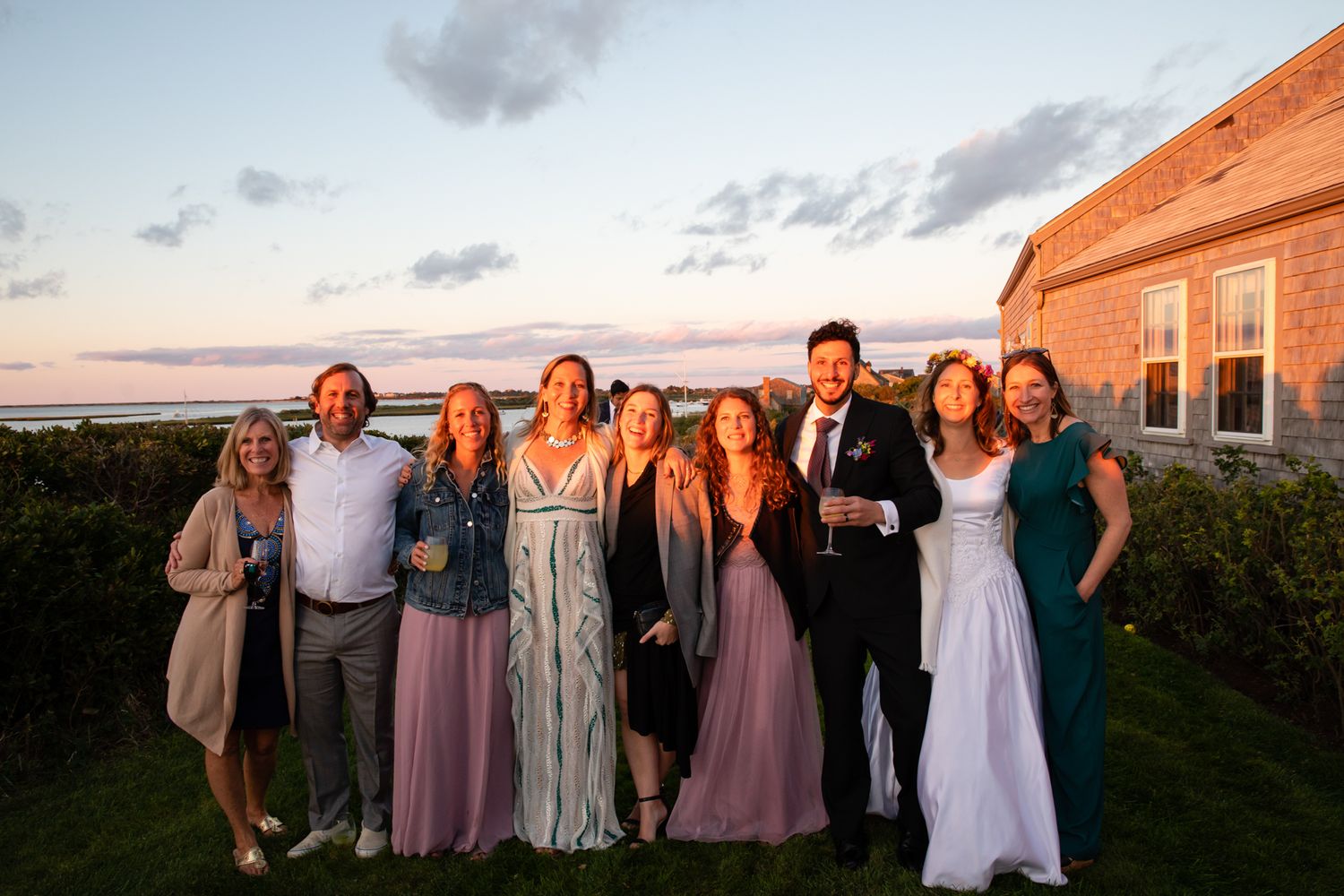 Wedding party poses together at sunset in front of a coastal building.