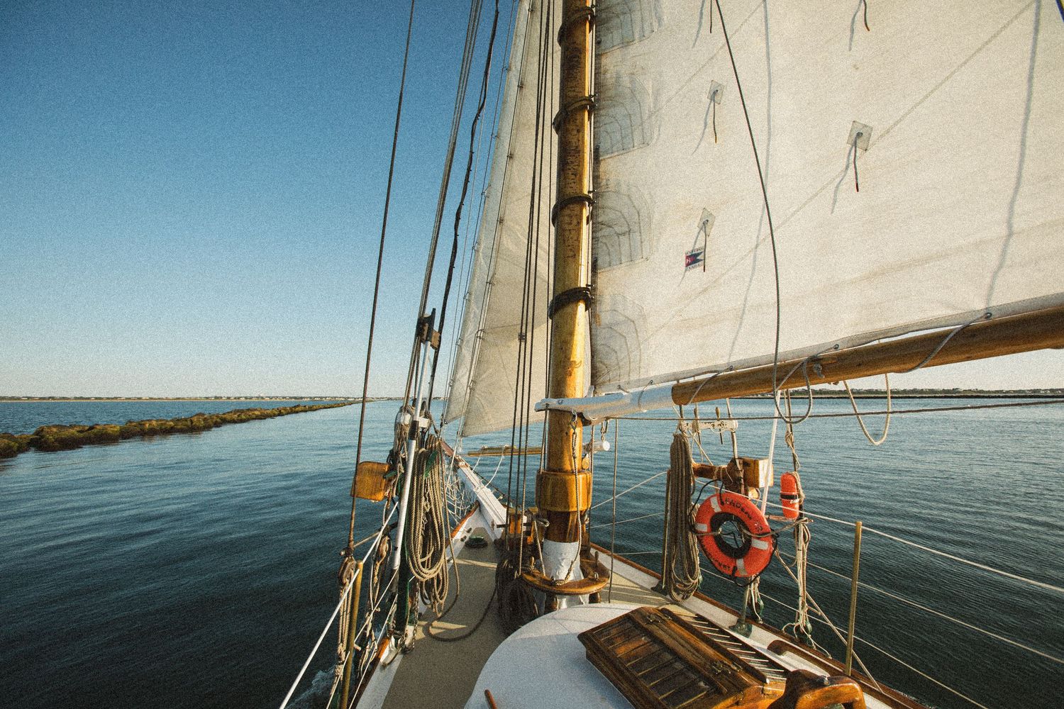 View of sailboat rigging and white sails against clear blue skies on calm waters.