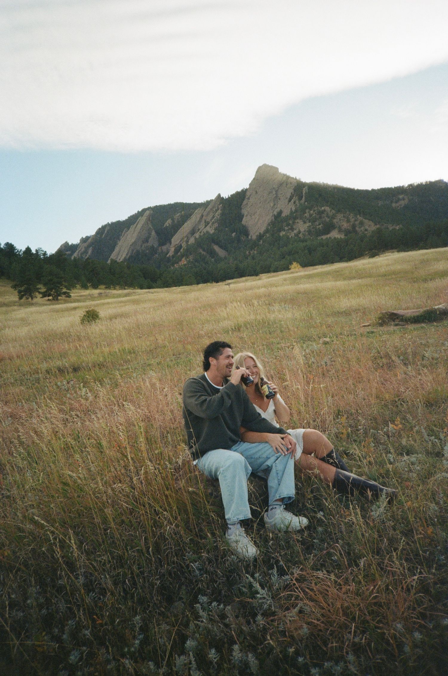 Couple relaxes in a meadow with the iconic Flatirons rock formation of Boulder, Colorado in the background.