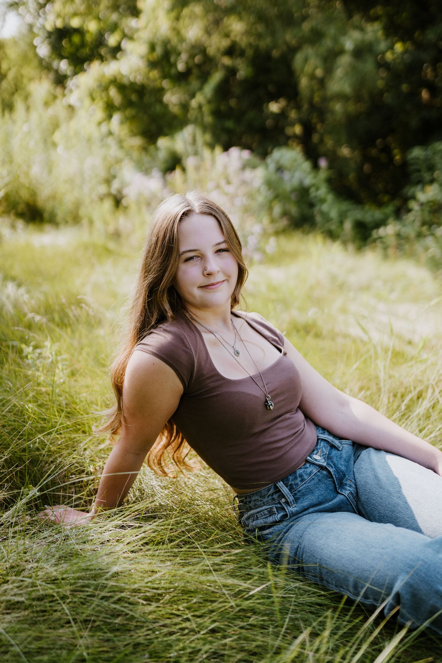 Casual summer portrait of someone sitting in sunlit meadow grass.