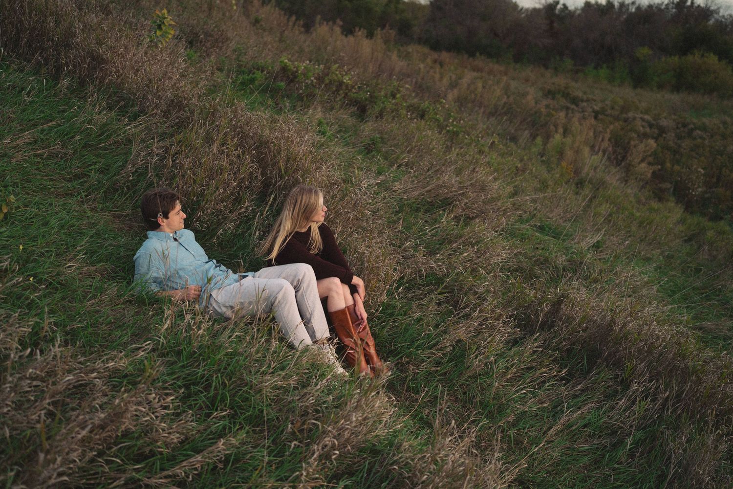 A couple relaxing together on a grassy hillside during an outdoor photo session.