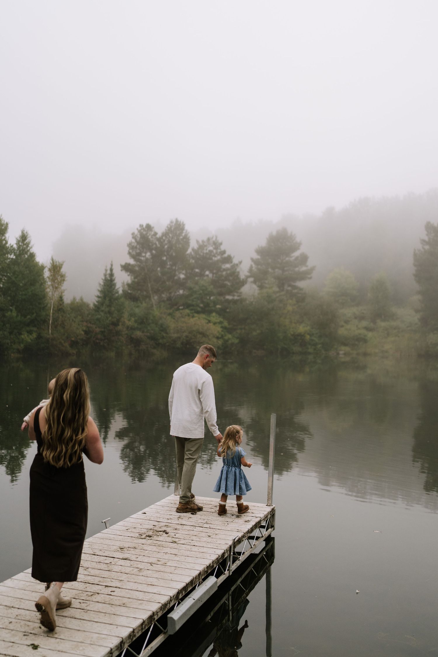 People gathered on a wooden dock overlooking a serene misty lake surrounded by trees.