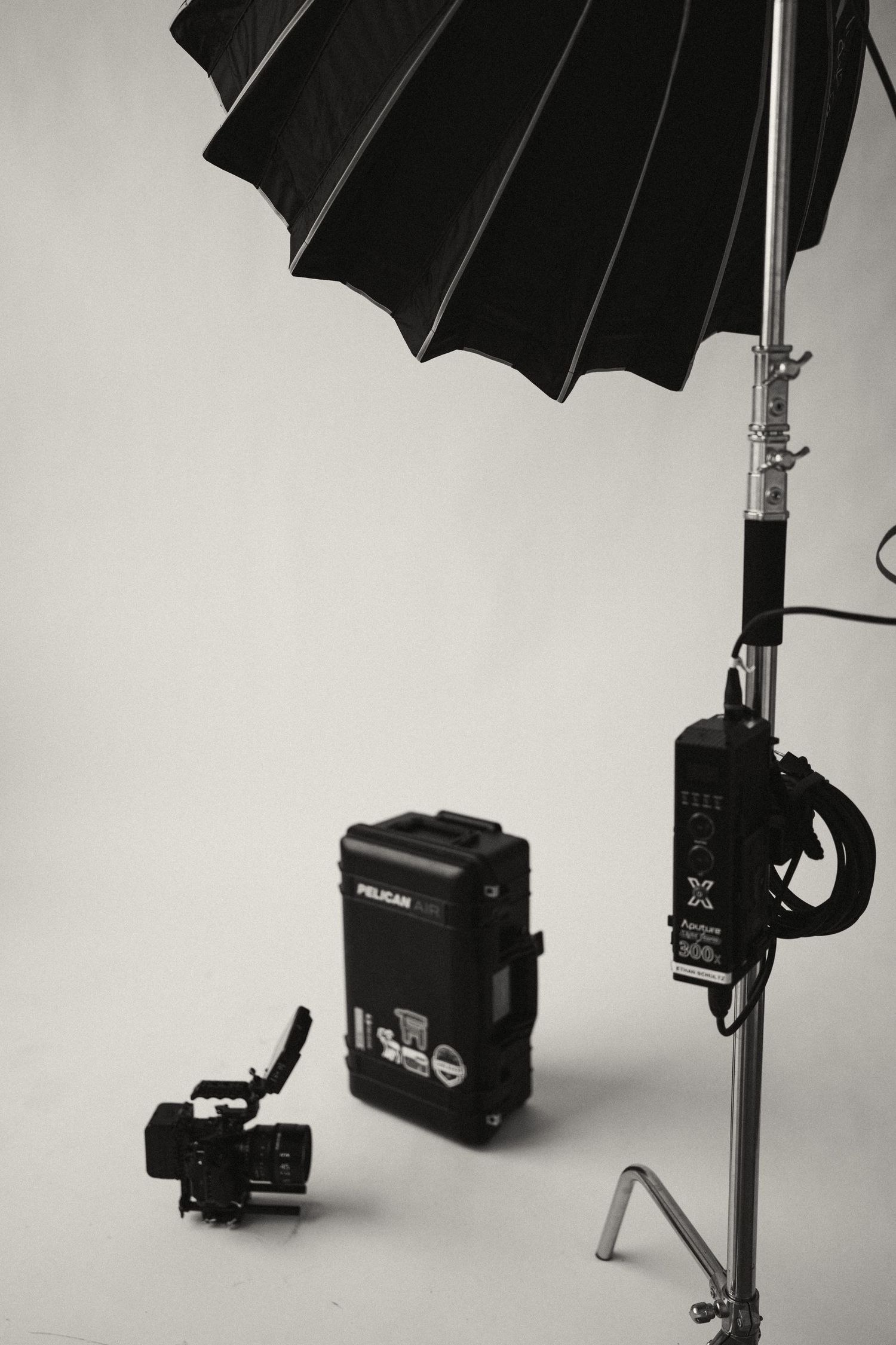 Studio lighting equipment setup with black umbrella and flash units against white background.