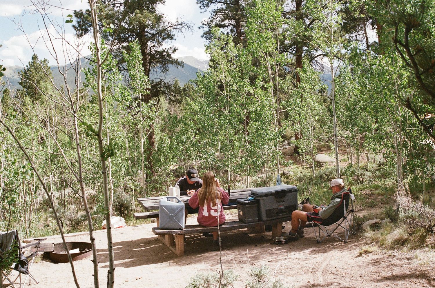 Rocky mountain campsite with scattered tents and equipment among pine trees.