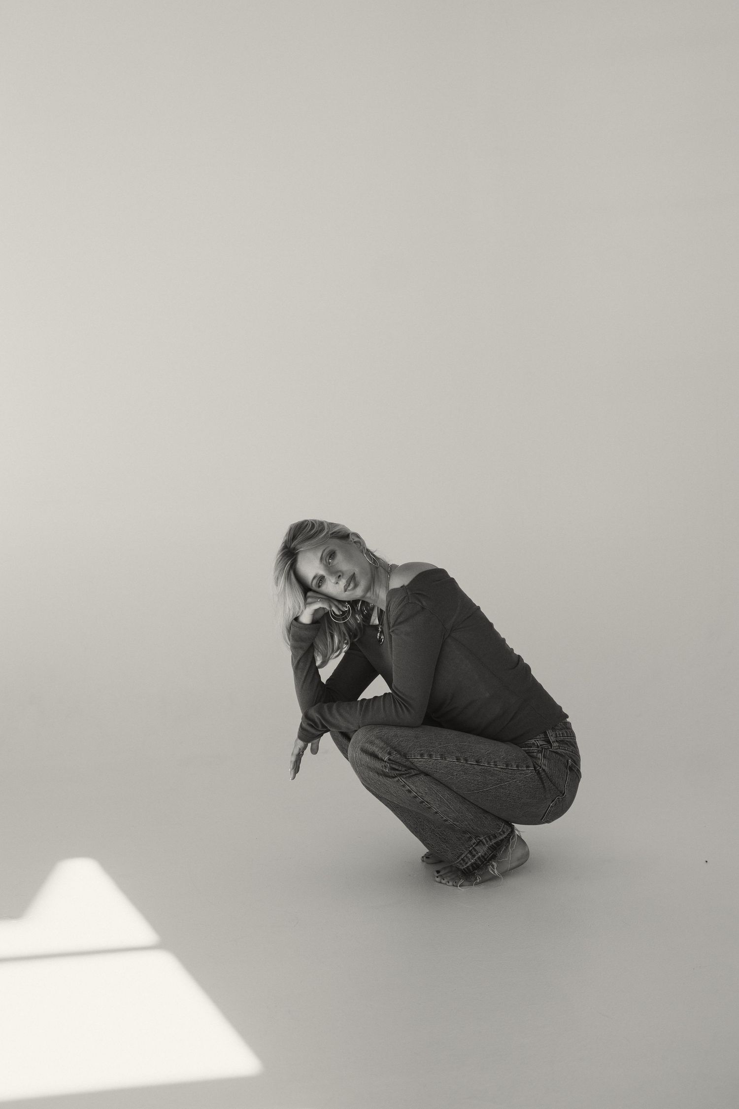 Black and white portrait of person crouching in casual pose with dramatic lighting.
