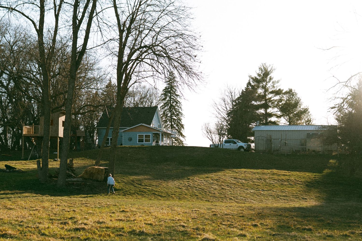 Rural landscape with houses and bare trees on a hillside at sunset.