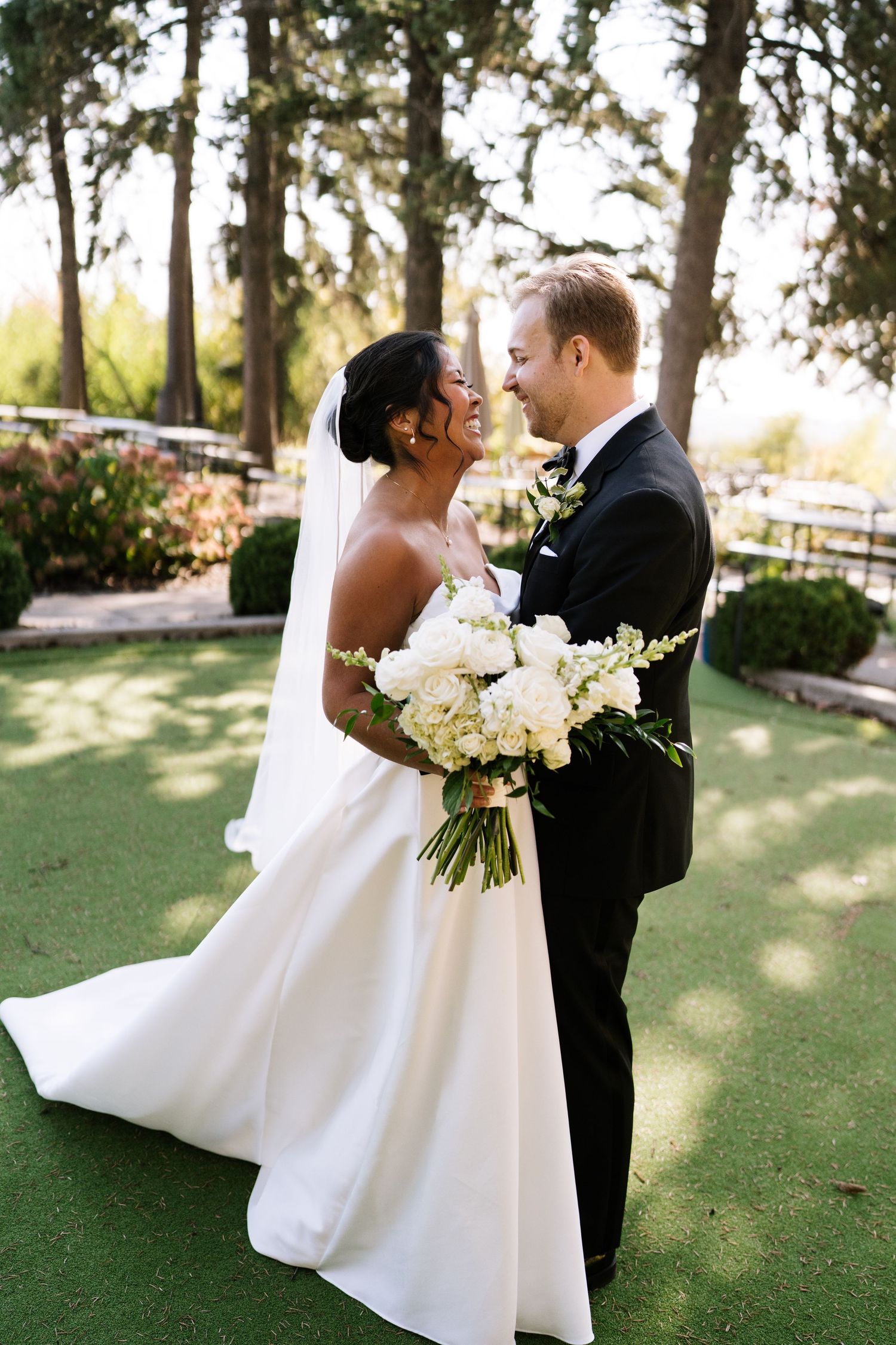 Romantic wedding portrait with bride holding white bouquet outdoors on a sunny day.