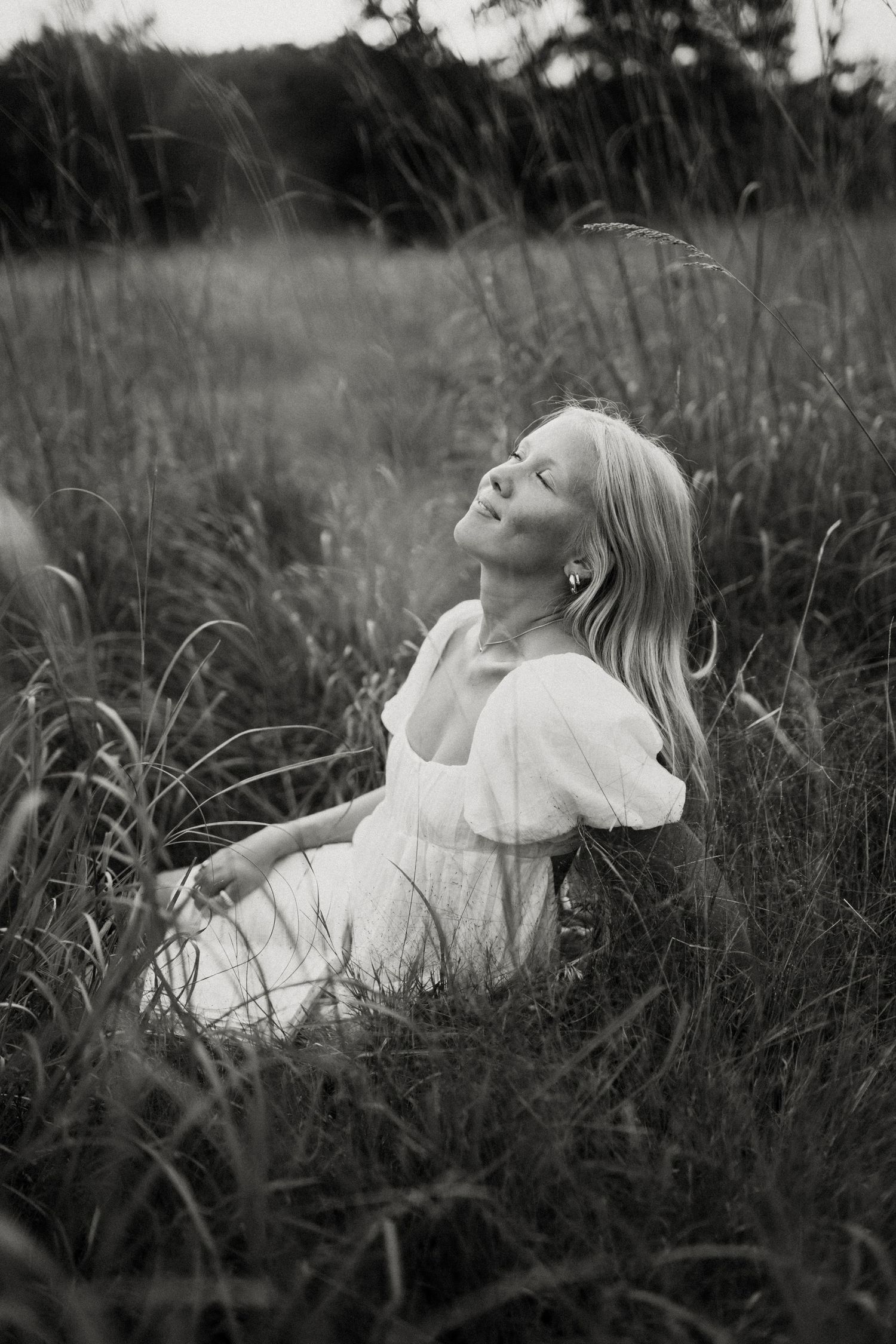 Black and white portrait of someone relaxing in a field of tall grass wearing a white dress.