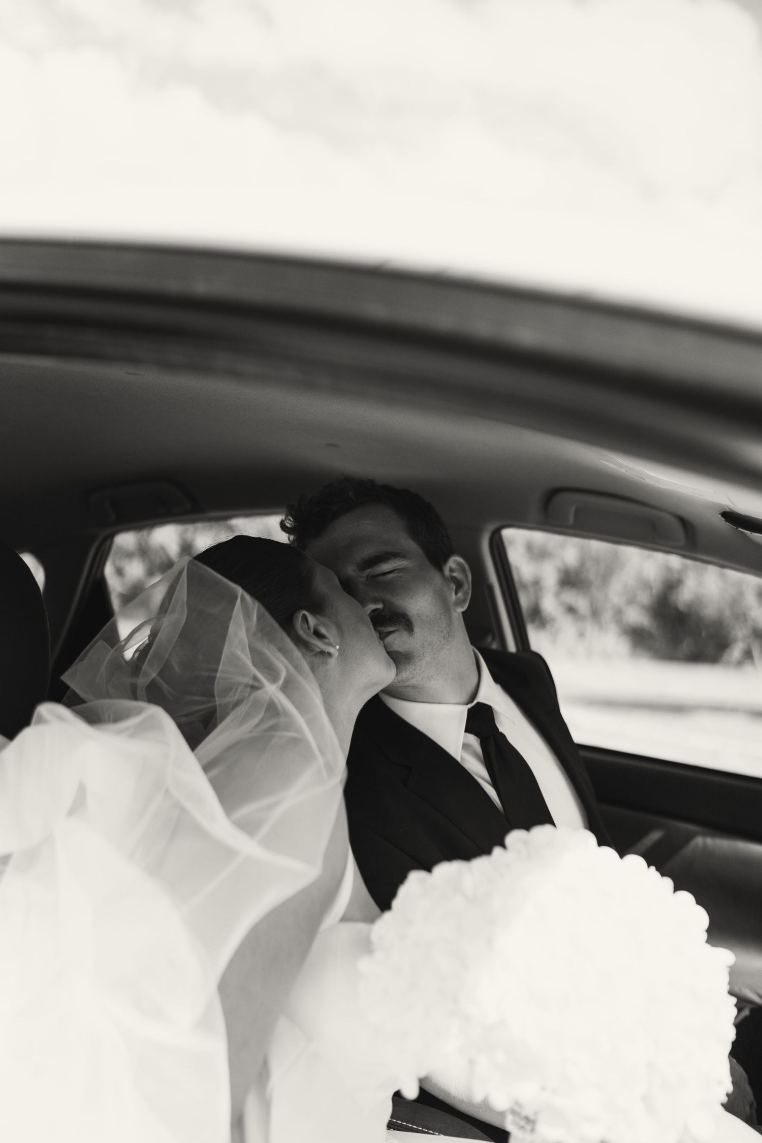 Black and white photo series capturing intimate moments of newlyweds in a car with flowing veil.