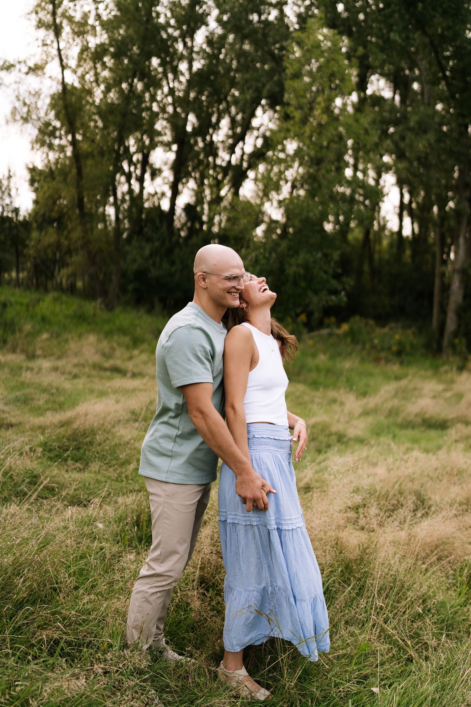 A tender embrace between a couple standing in tall grass with trees in the background.