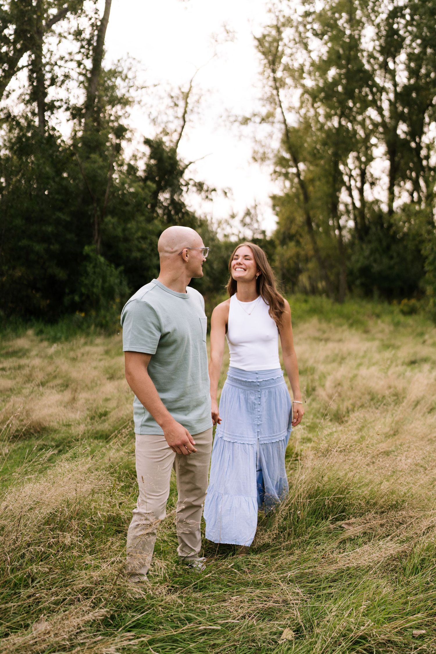 A couple shares a joyful moment while standing in a grassy field at sunset.
