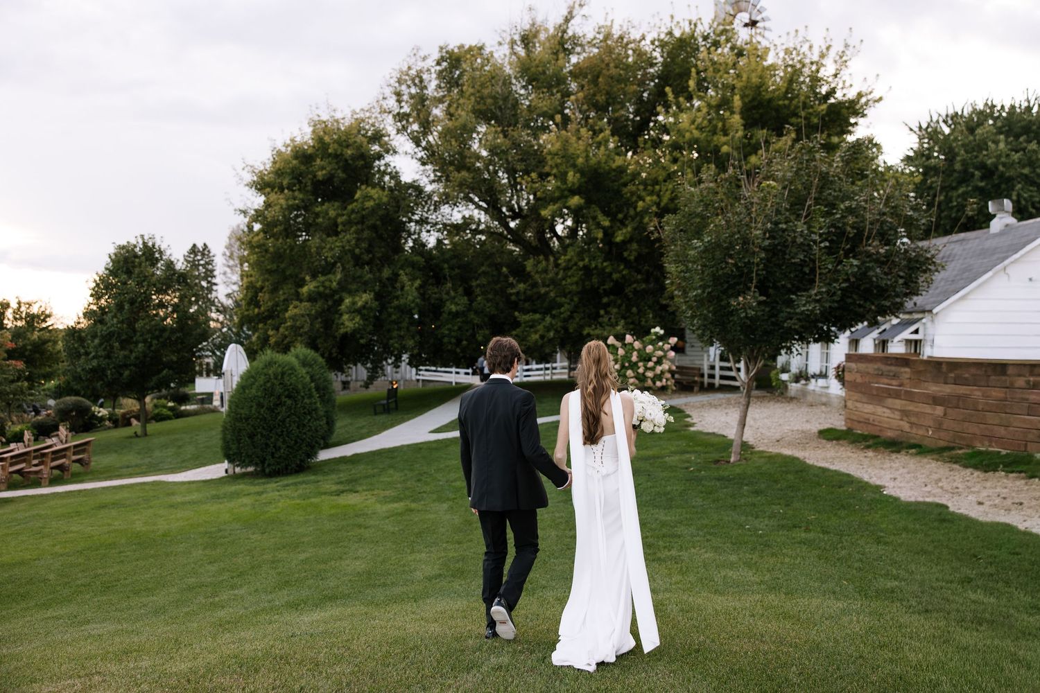 Couple walking together on a grassy path during their wedding day.