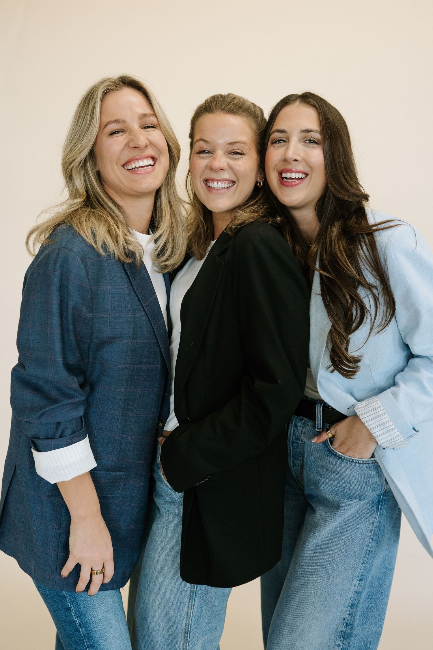 Three friends in denim and black clothing laughing and embracing together in a casual photoshoot.