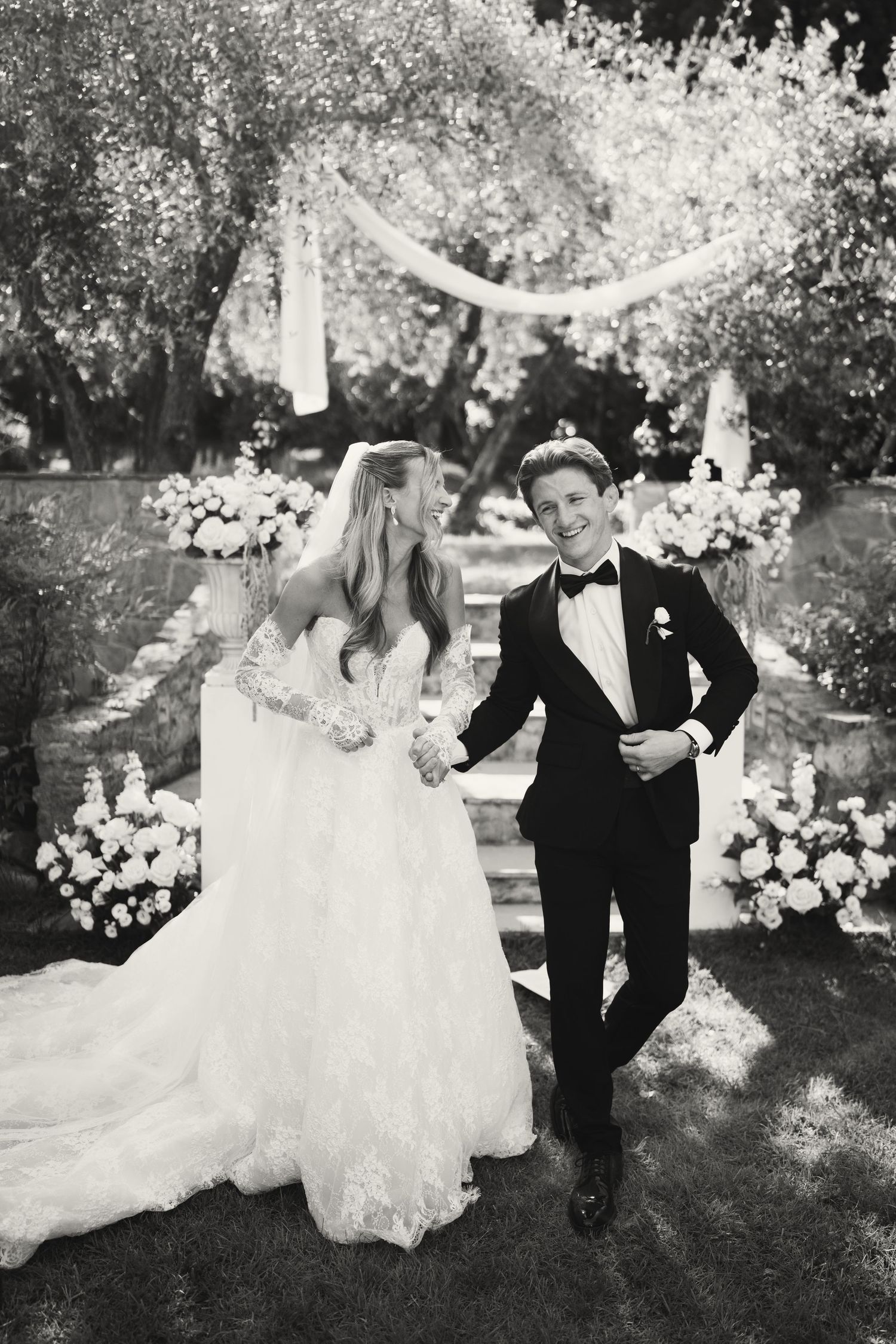 Black and white photo of a smiling bride and groom walking together outdoors after their wedding ceremony.