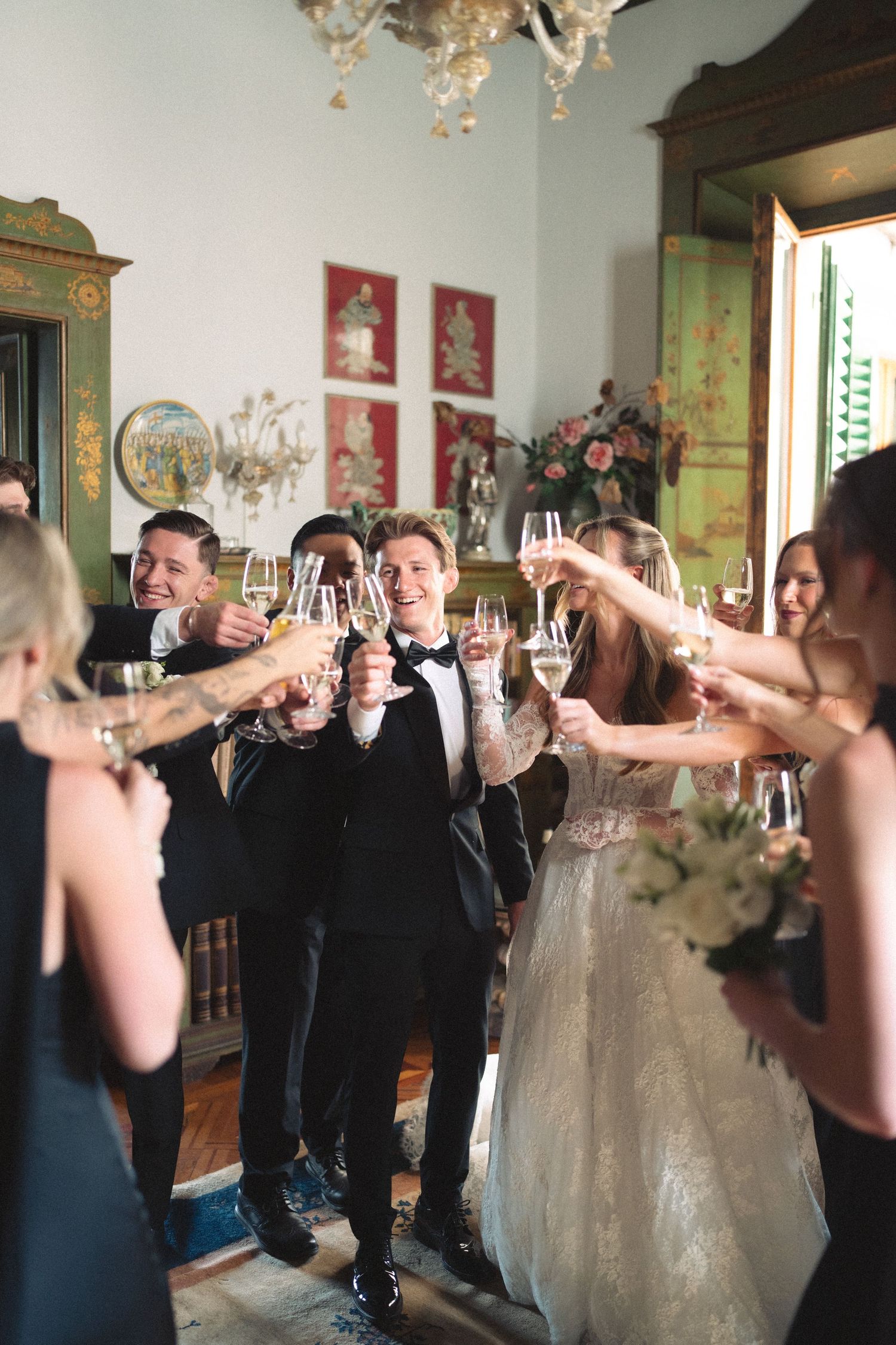 Bride and groom toasting champagne with wedding guests in an elegant villa reception room.