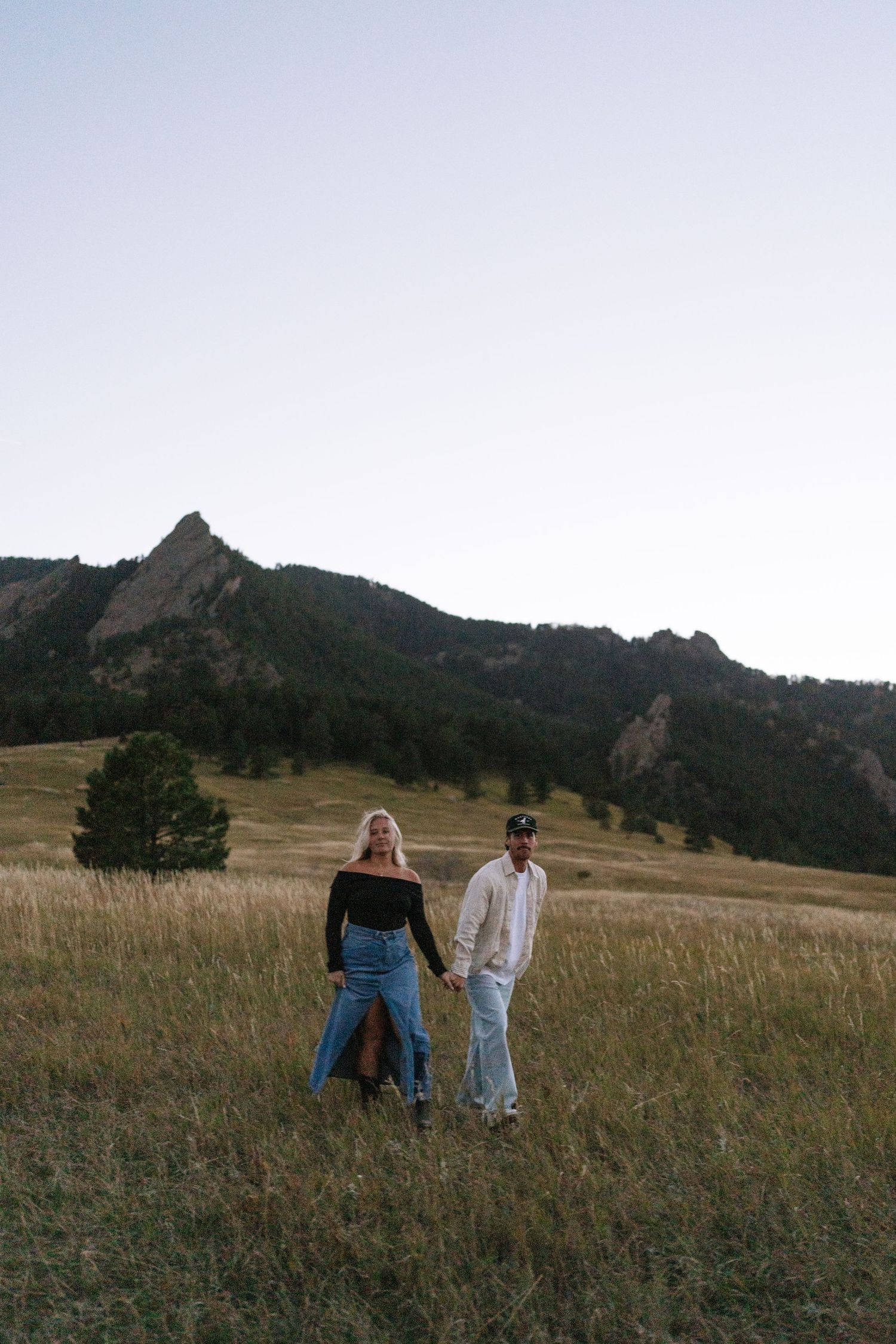 Couple walks through mountain meadow with dramatic peaks in background.