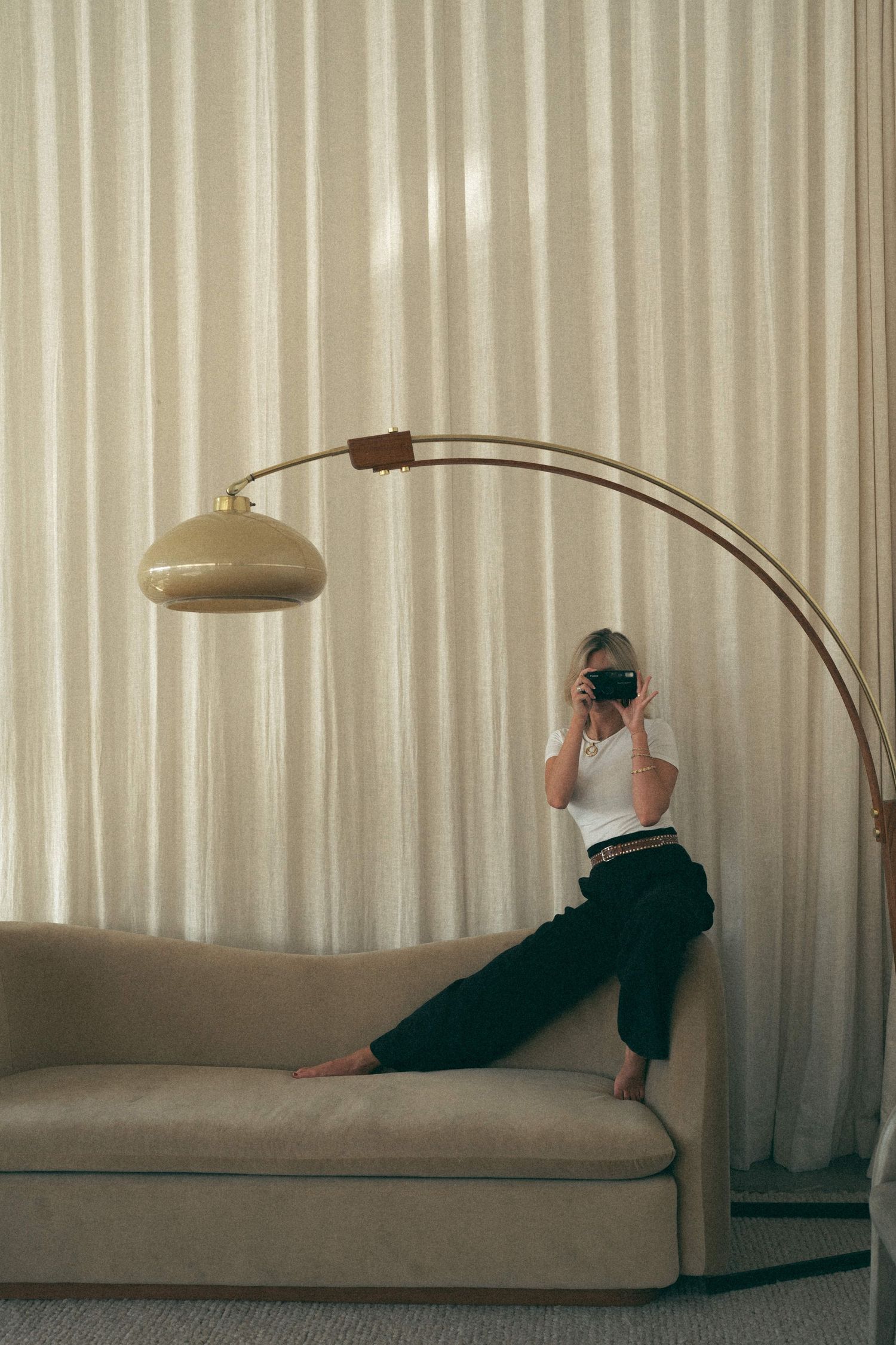 Minimalist photo series of person lounging on beige couch under arc lamp.