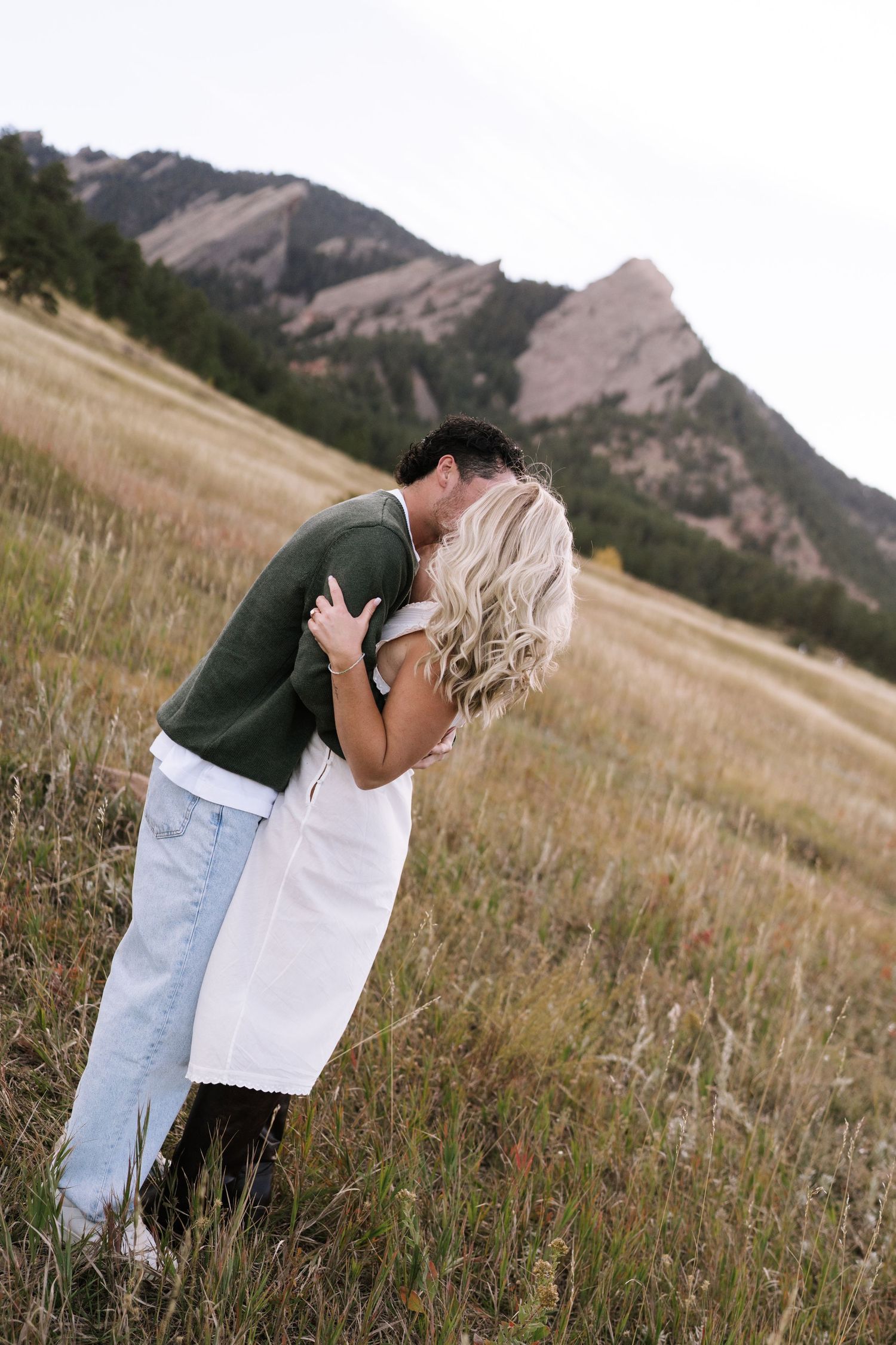 Couple embraces in a scenic mountain meadow during golden hour.
