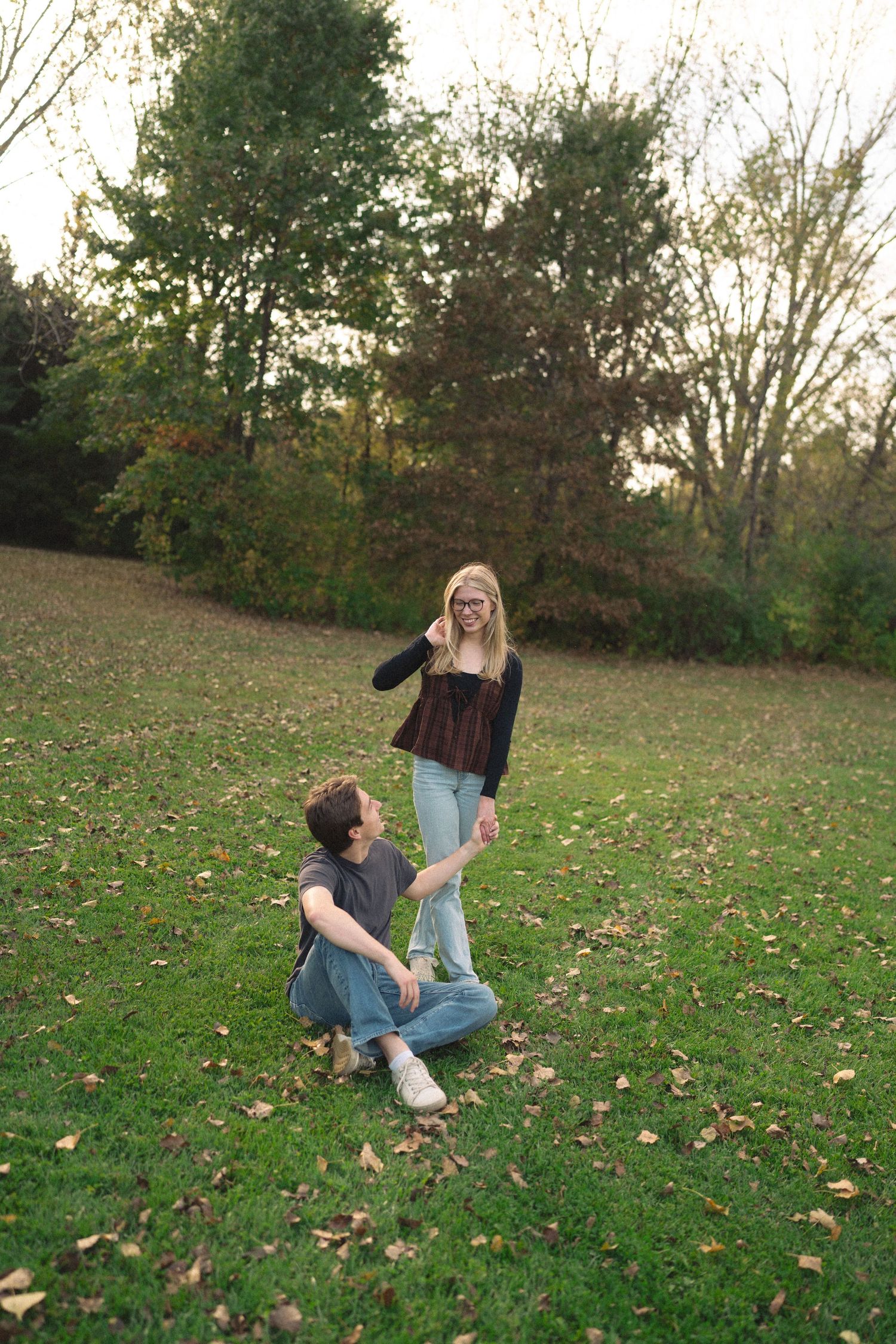 A couple playing and falling down together on an autumn lawn covered in leaves.