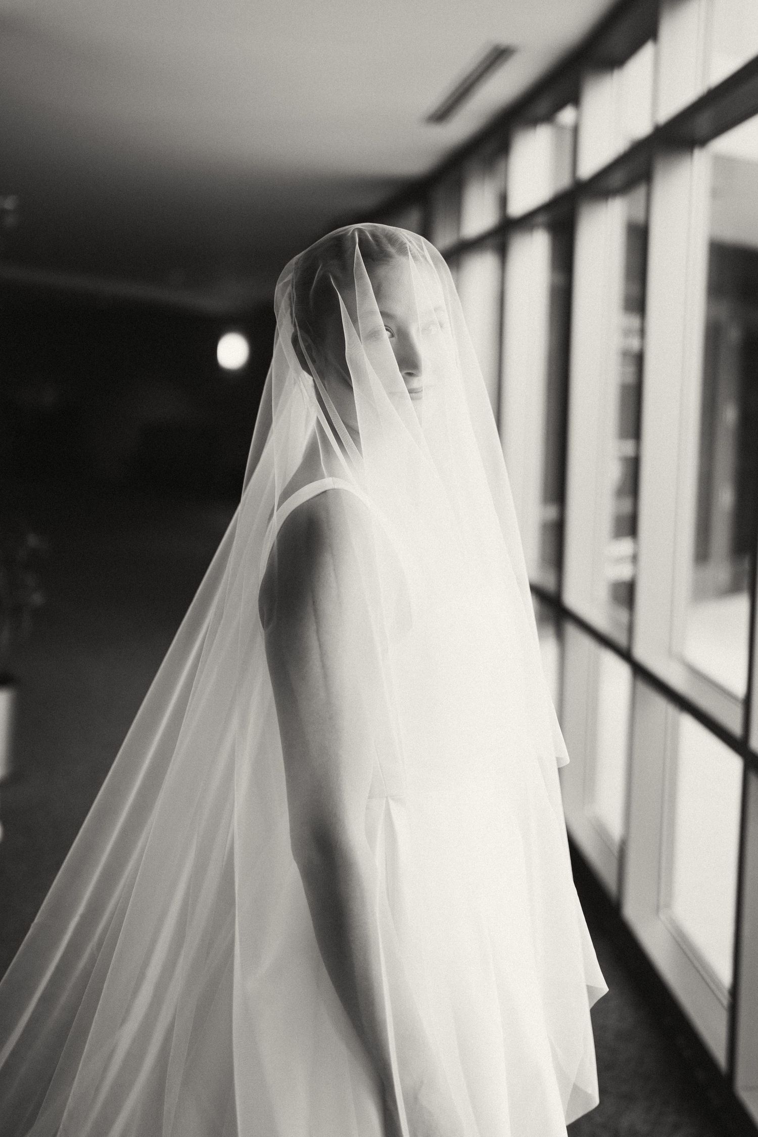Artistic black and white silhouette of a bride in her veil by a window.