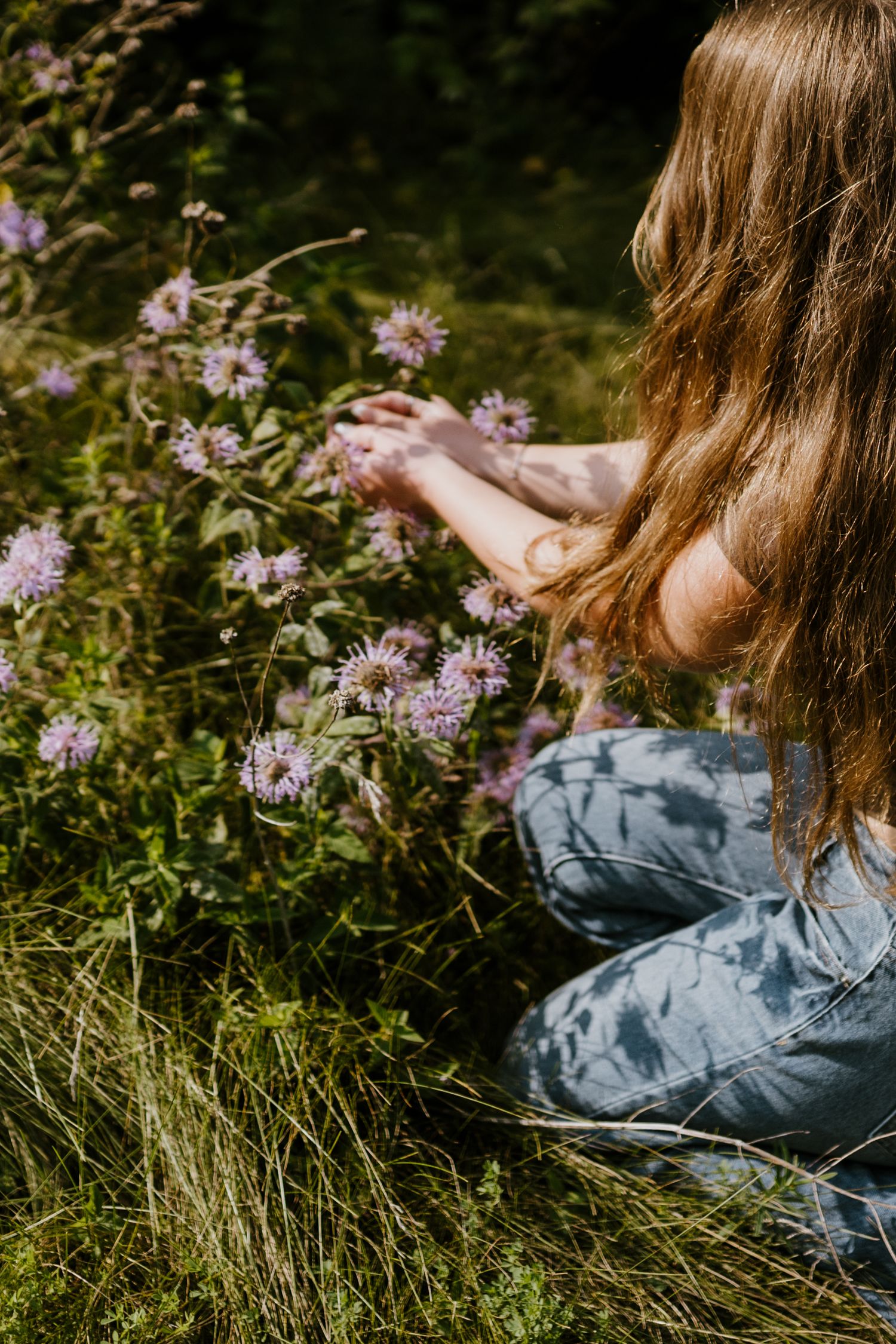 Artistic portrait in tall grass with purple wildflowers creates a moody natural setting.