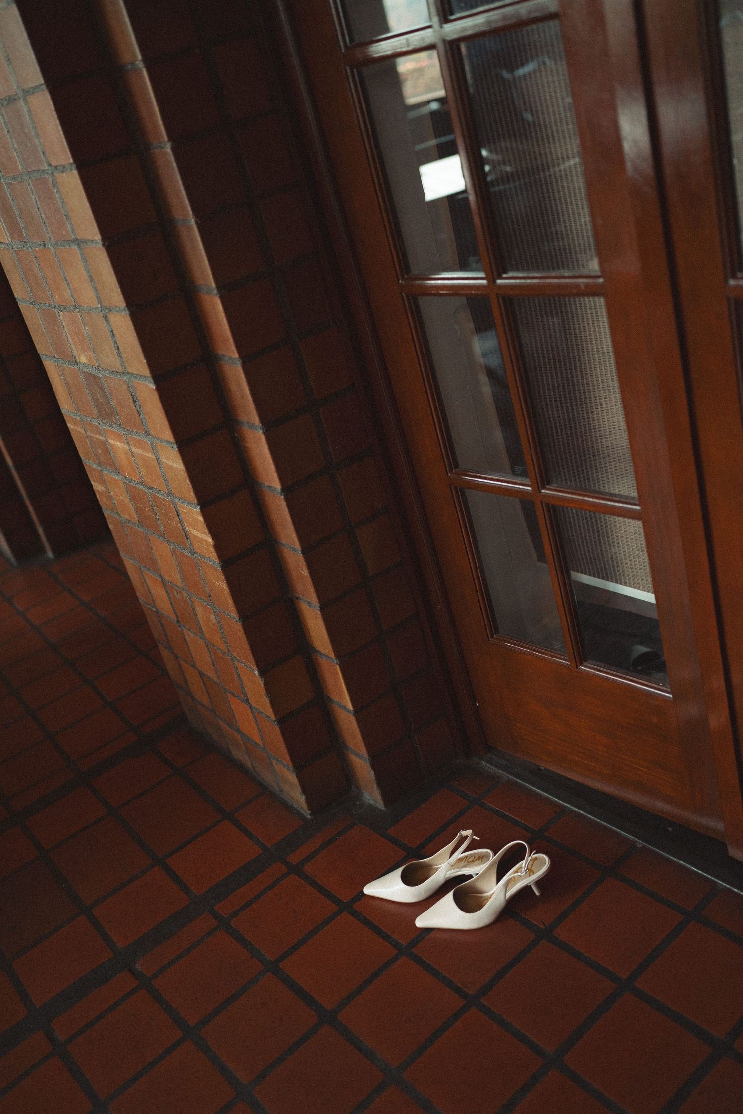 White shoes placed neatly at a wooden door entrance with terracotta floor tiles.