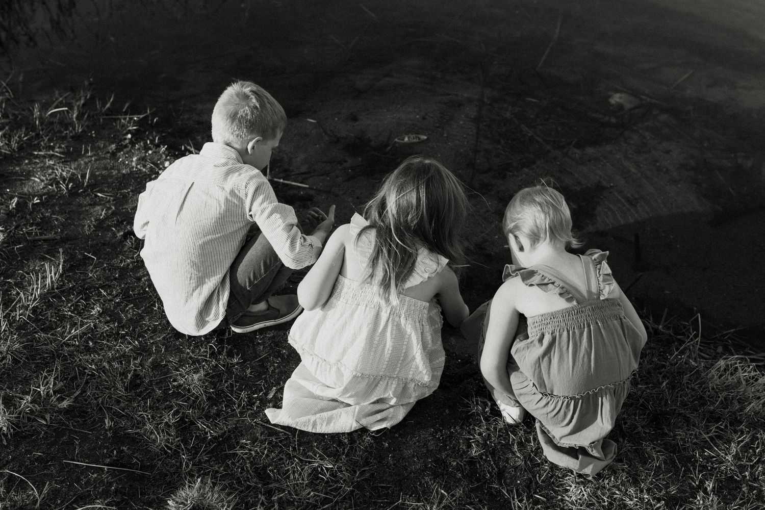 Three children sitting together on a grassy slope in black and white.