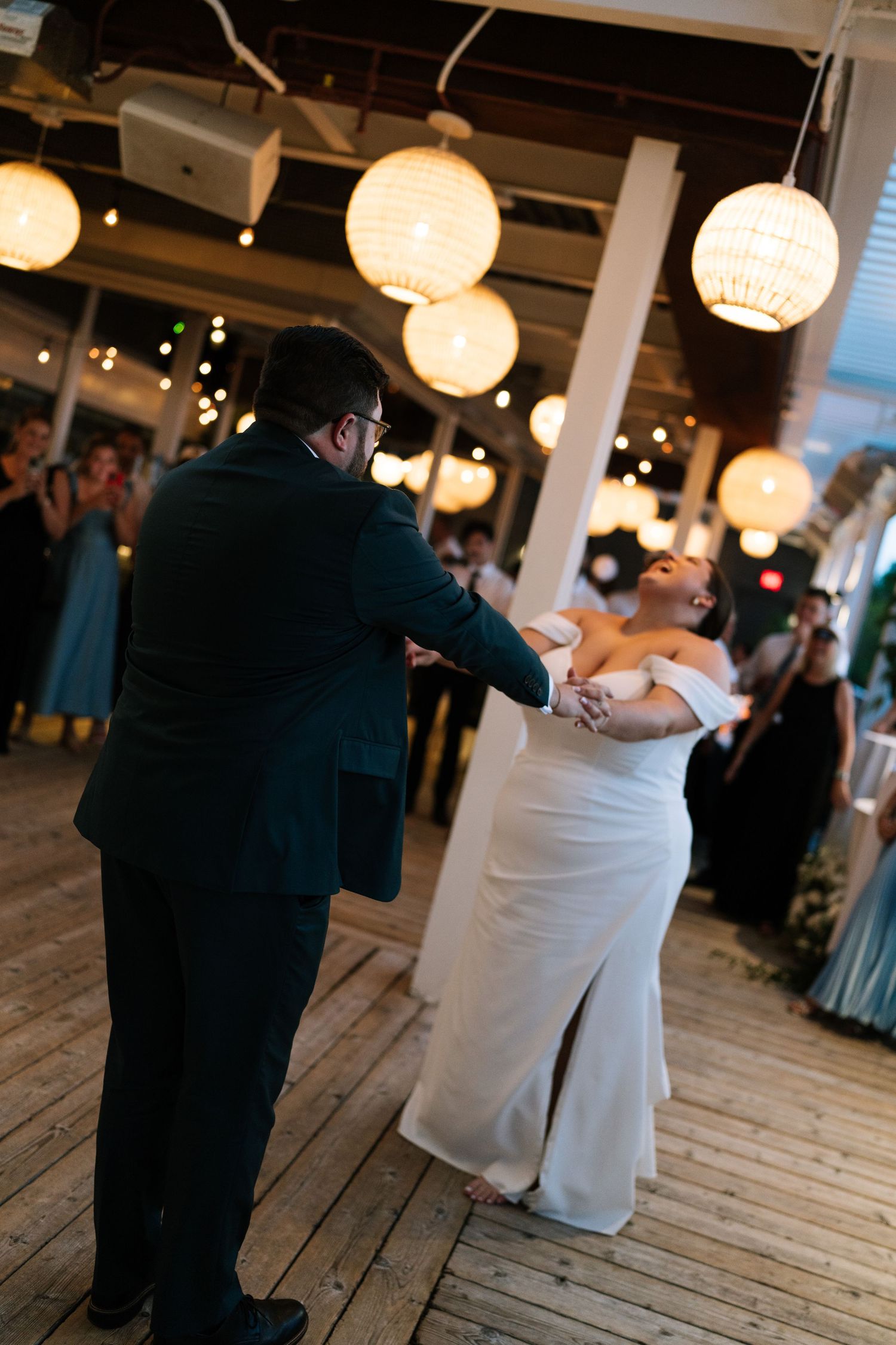 Couple dancing together at a wedding reception under paper lantern lighting on a wooden floor.